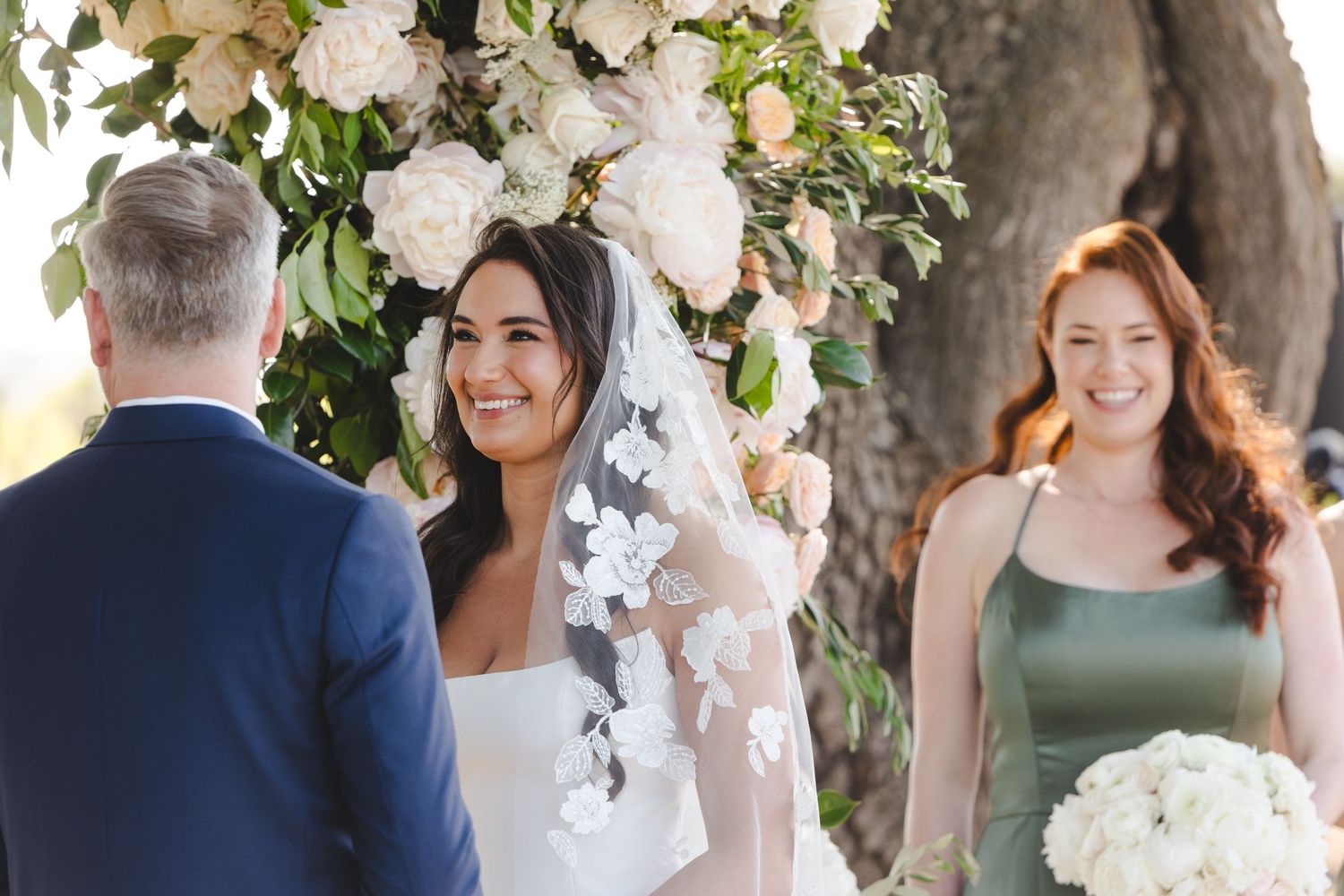 Wedding party gathering under tree canopy with elegant floral arrangements.