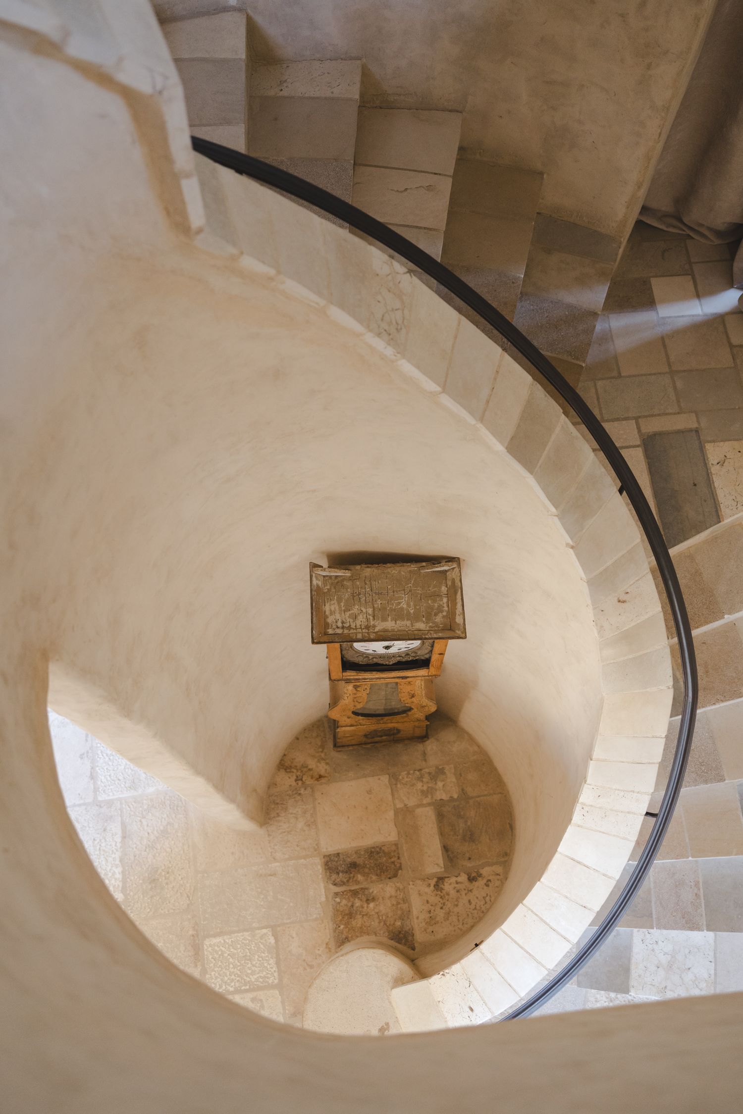 Looking down a spiral stone staircase with wooden furniture piece at the bottom creating an architectural vortex effect.
