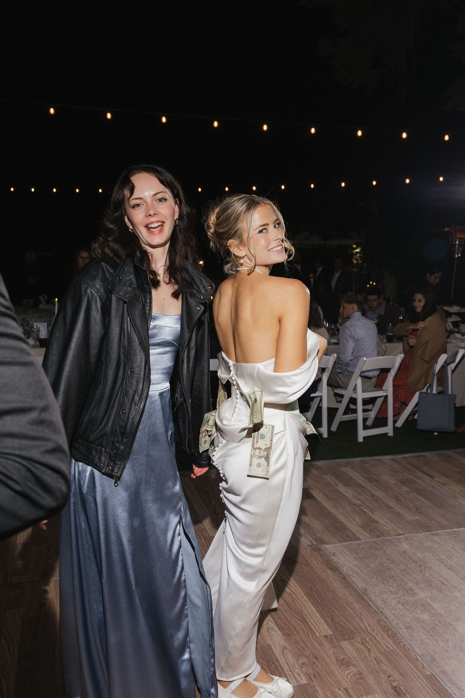 Wedding guests dance and celebrate on a wooden dance floor under twinkling string lights at an evening reception.