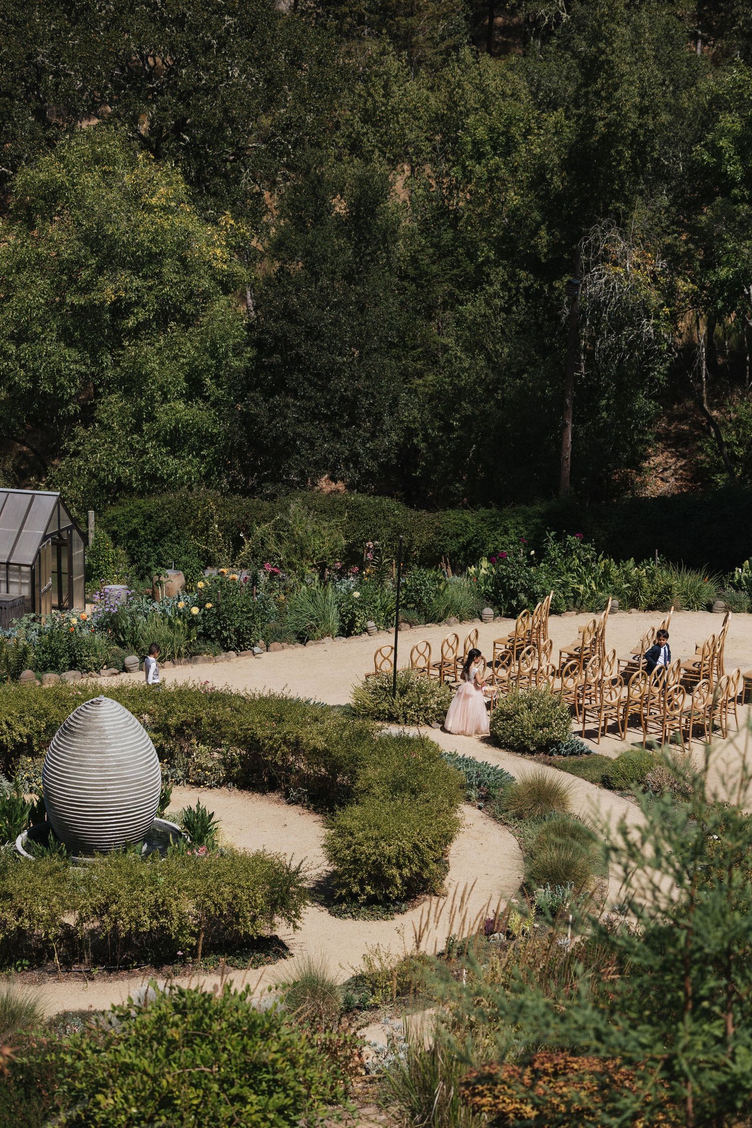 Winding garden path with wooden chairs arranged along a curved walkway surrounded by lush greenery.