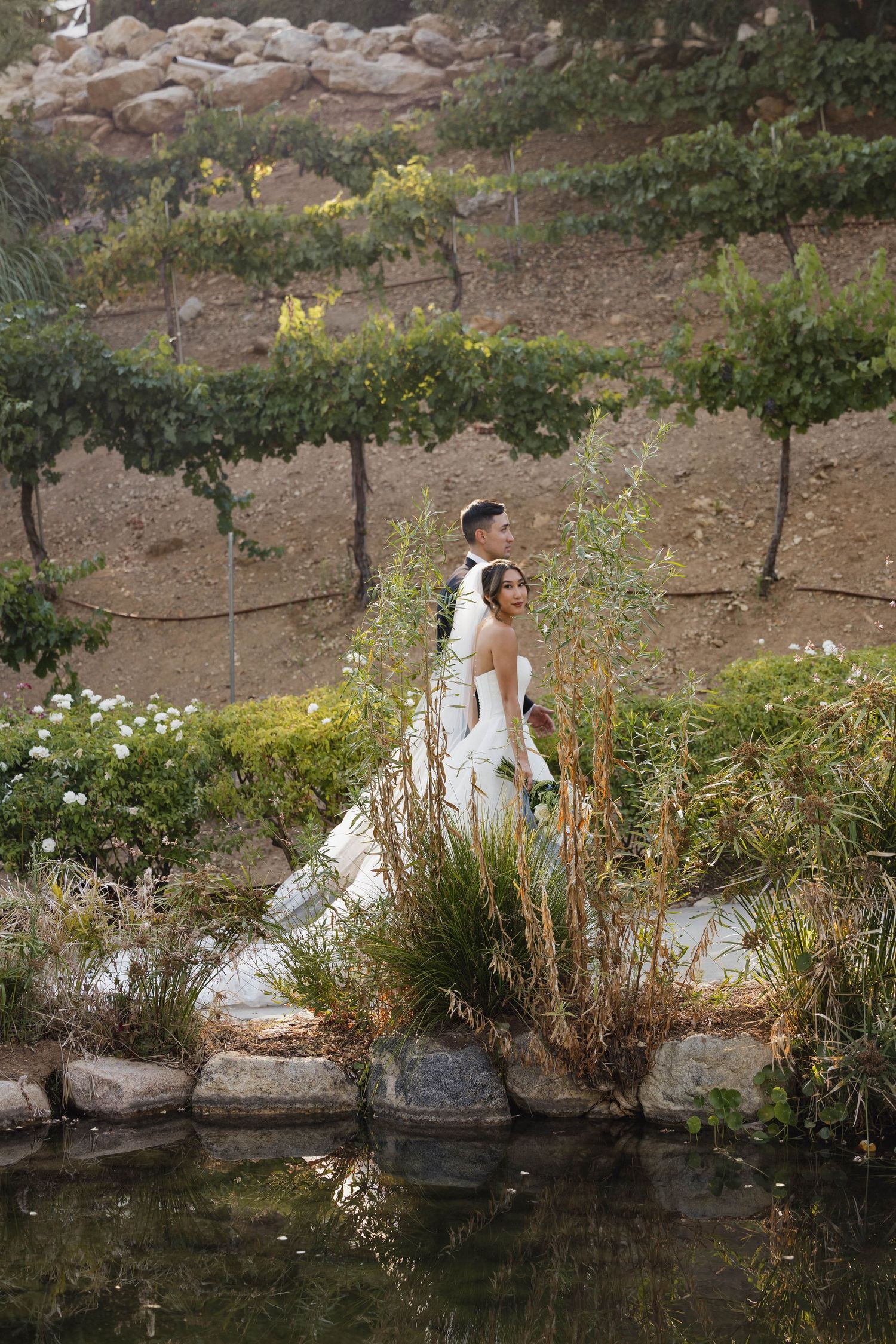 A scenic outdoor photo session with a long white dress against a natural pond backdrop and greenery.