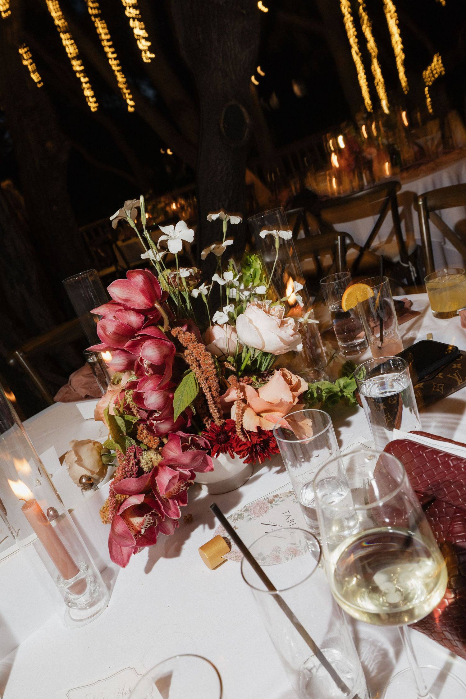 Elegant wedding reception table centerpiece with pink and white flowers, candles, and wine glasses at night.