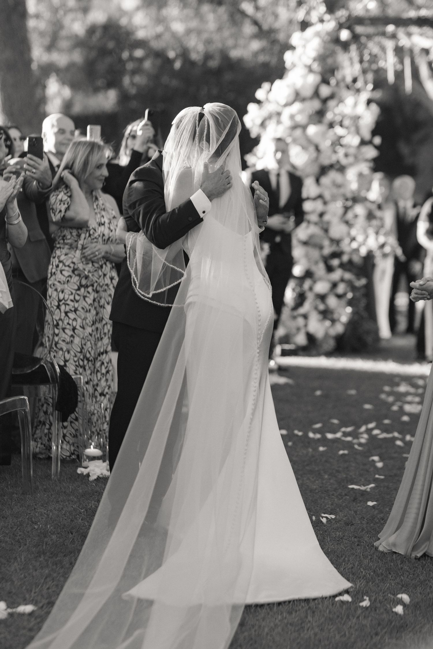 Black and white photo of a bride and groom walking down the aisle at an outdoor wedding ceremony.