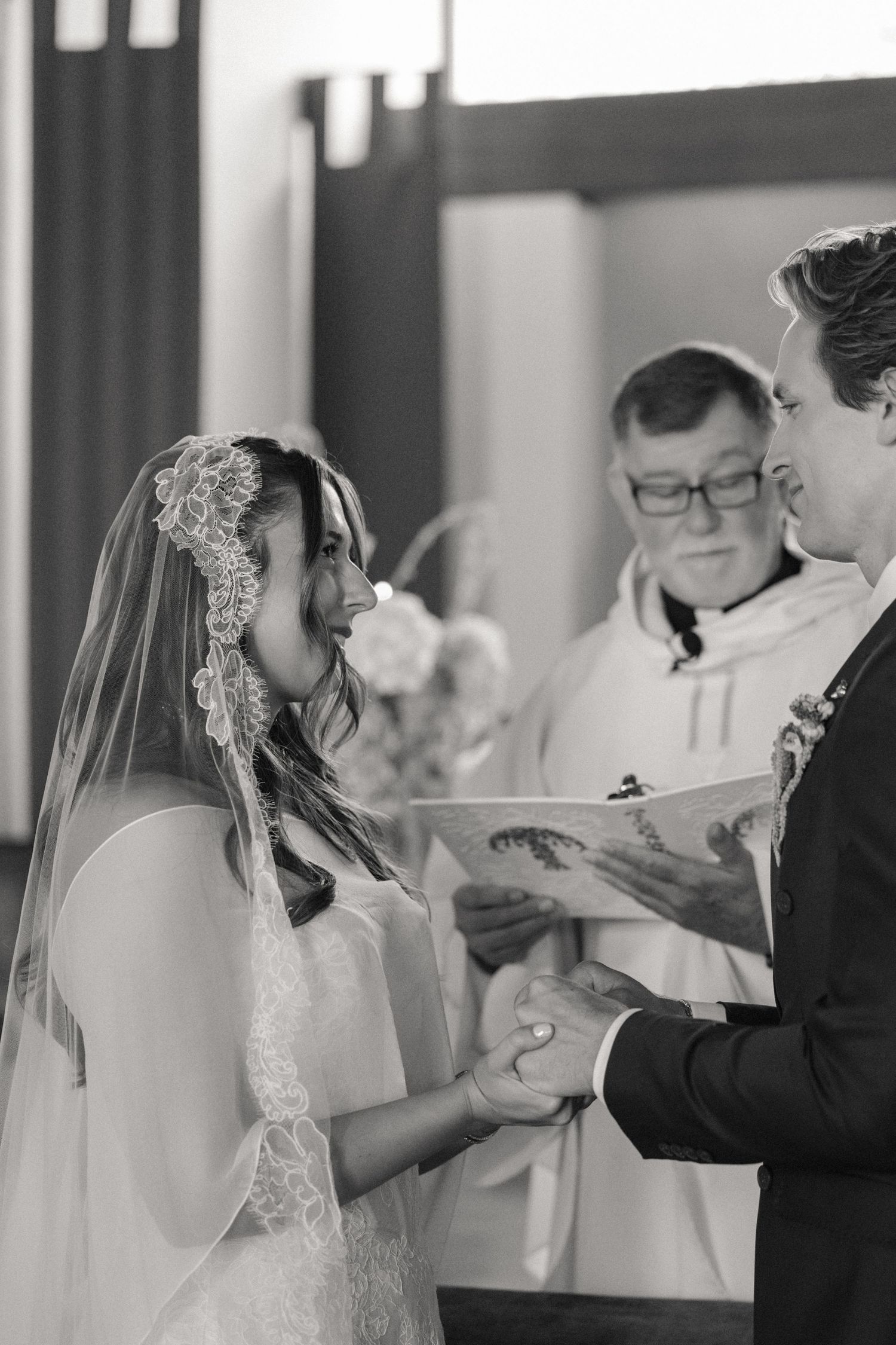 Black and white photo of a bride and groom exchanging vows at a church wedding ceremony with officiant.