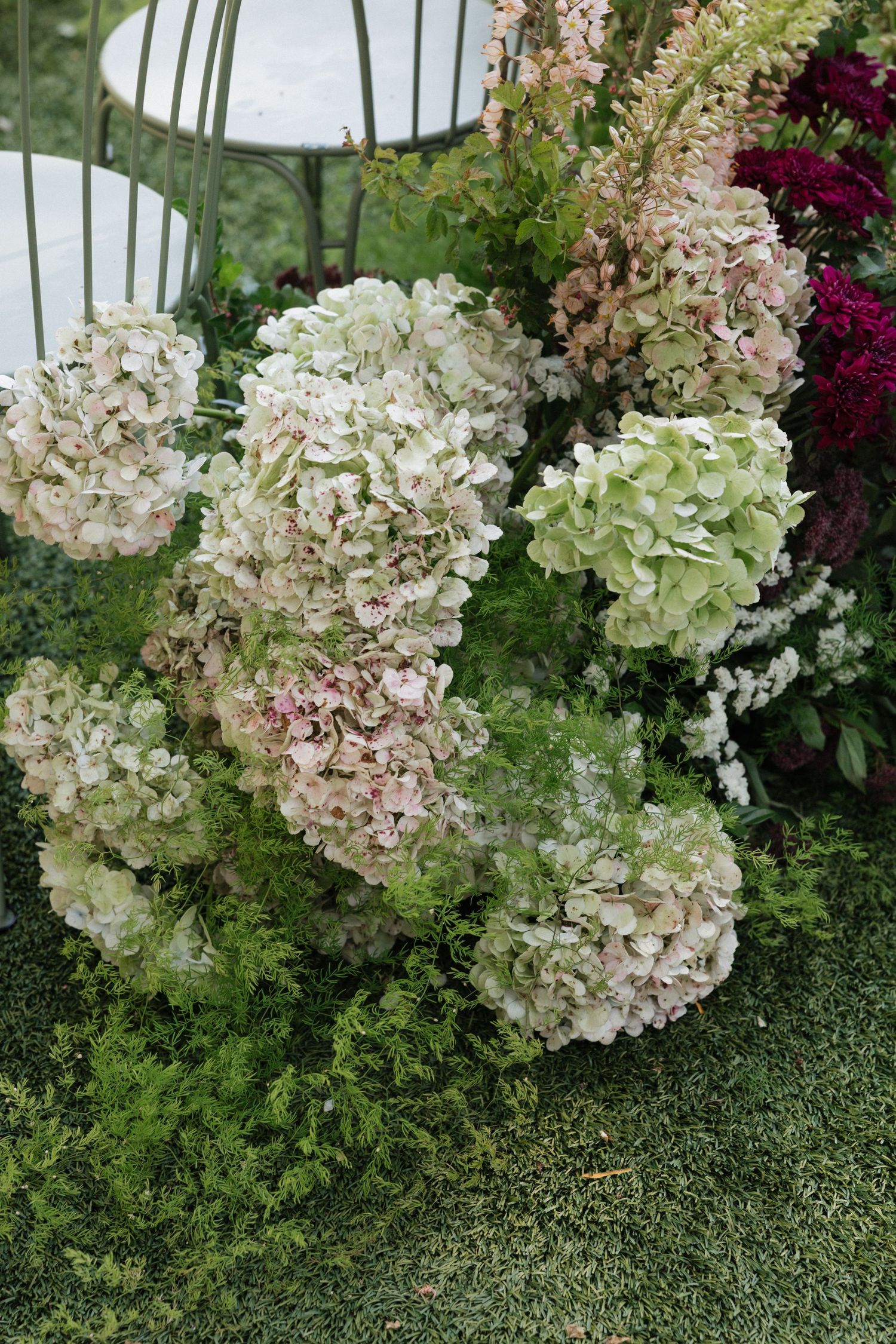 Lush floral arrangement featuring white and pink hydrangeas with green foliage on a grass surface.