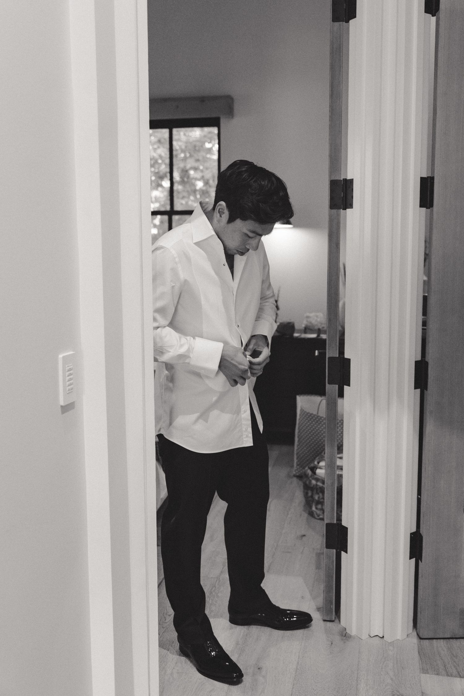 A person in a white shirt and dark pants bends down to examine something near a doorway.