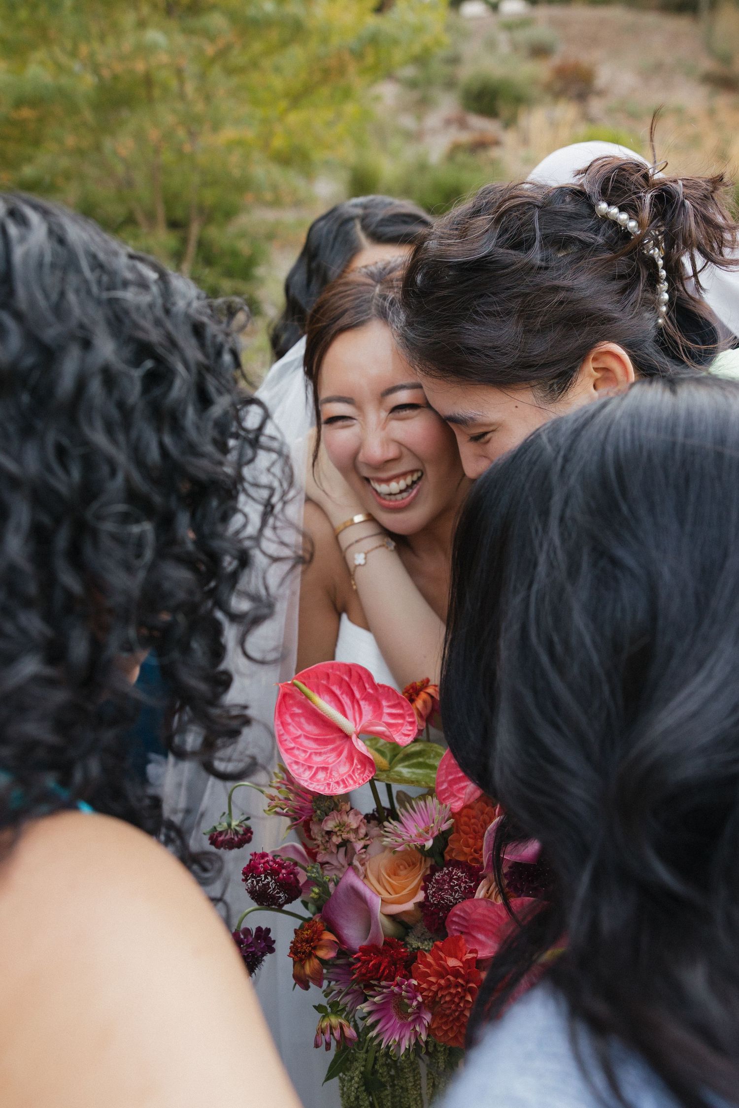 Wedding party members share a joyful moment with vibrant red and pink flowers in an outdoor setting.