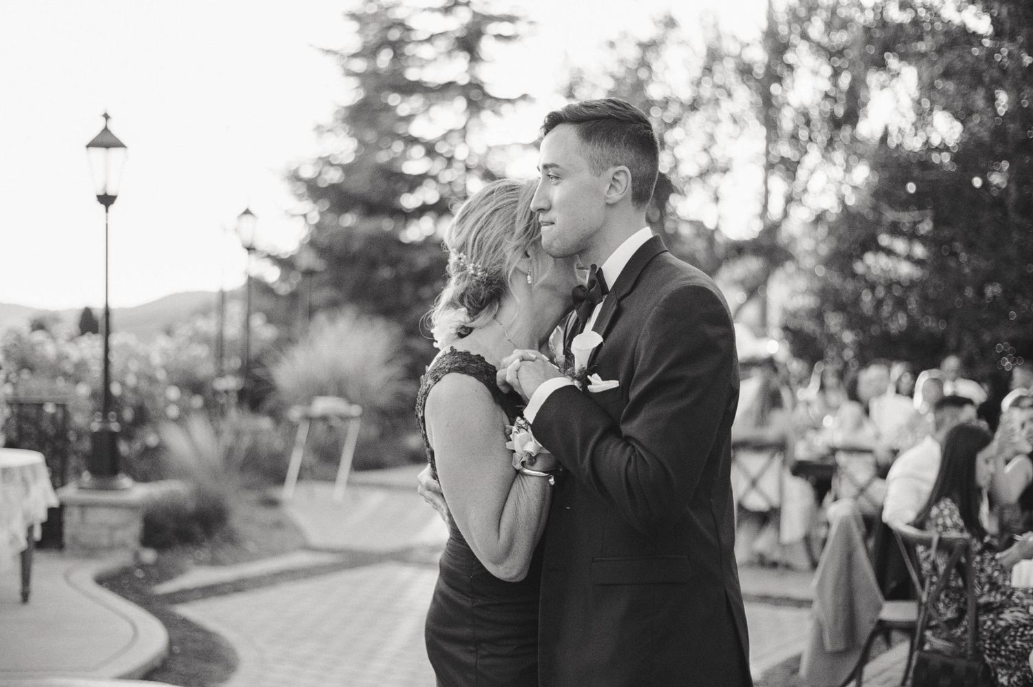 Black and white candid moment at an outdoor wedding reception with lamp post in background.