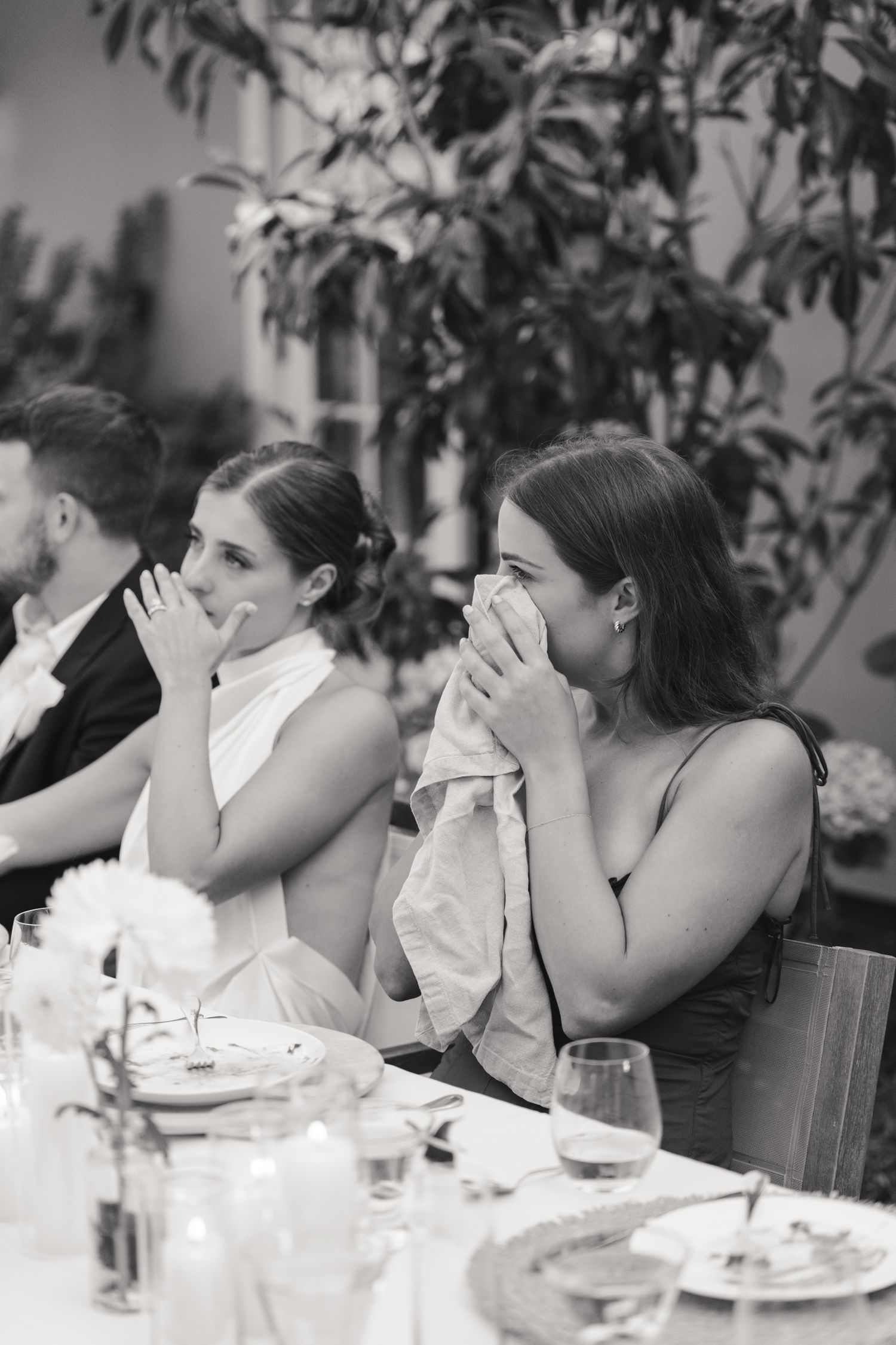 Emotional guests wipe tears with napkins while seated at an elegant outdoor wedding reception table.
