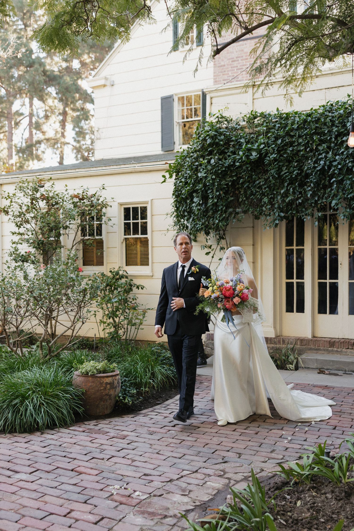 Wedding couple shares a private moment on brick patio surrounded by lush greenery.