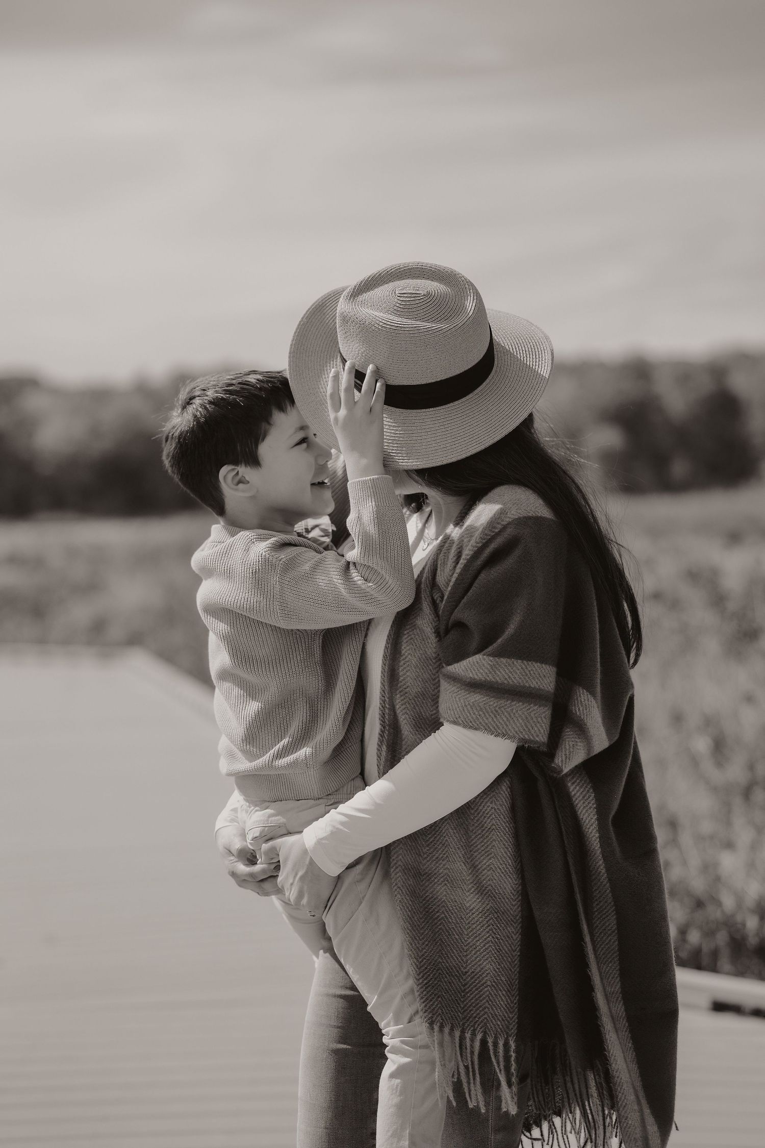 Black and white photo of a tender moment between parent and child wearing a hat in an outdoor setting.