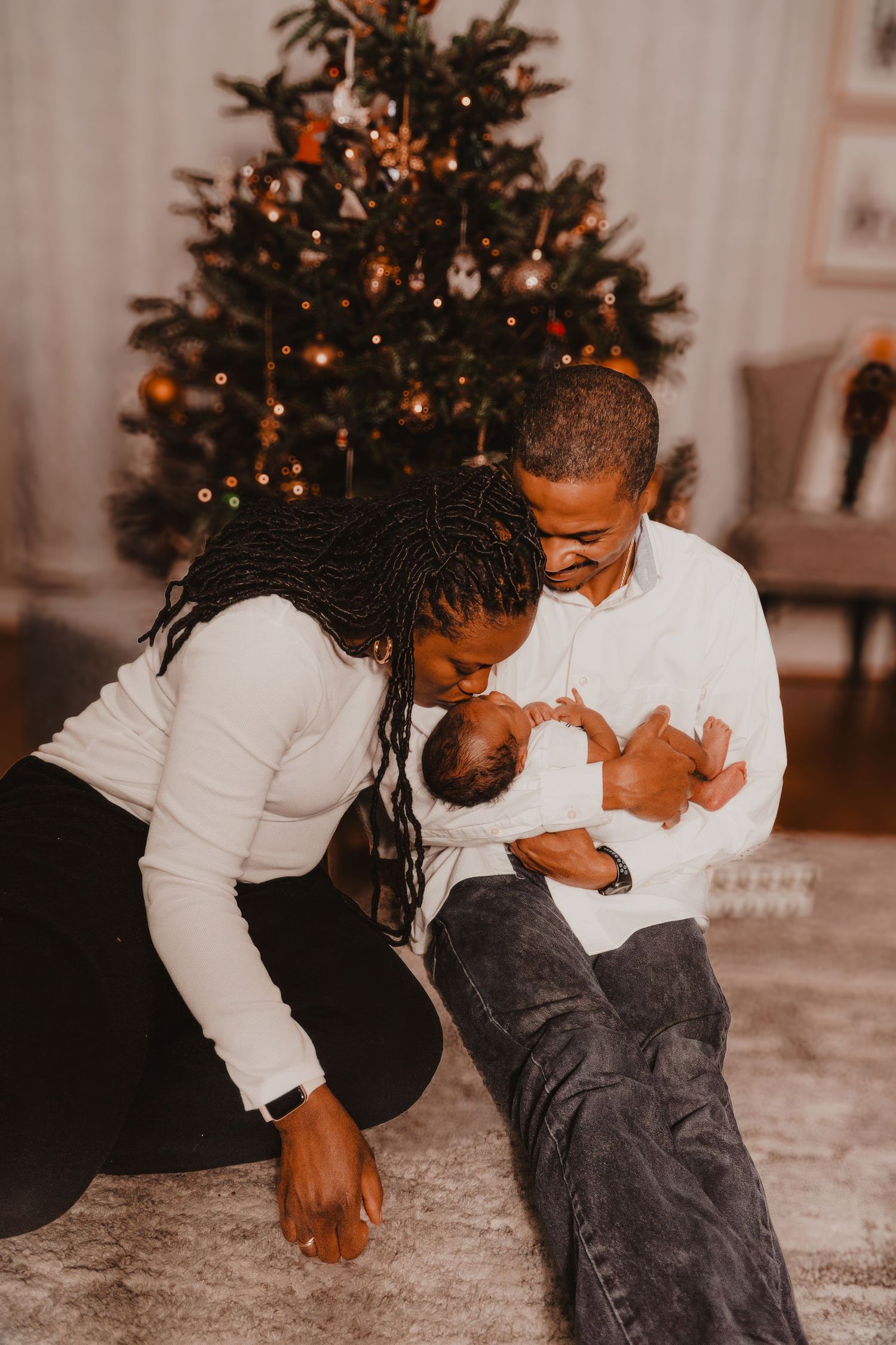 A family sharing intimate moments with their baby in front of a decorated Christmas tree.