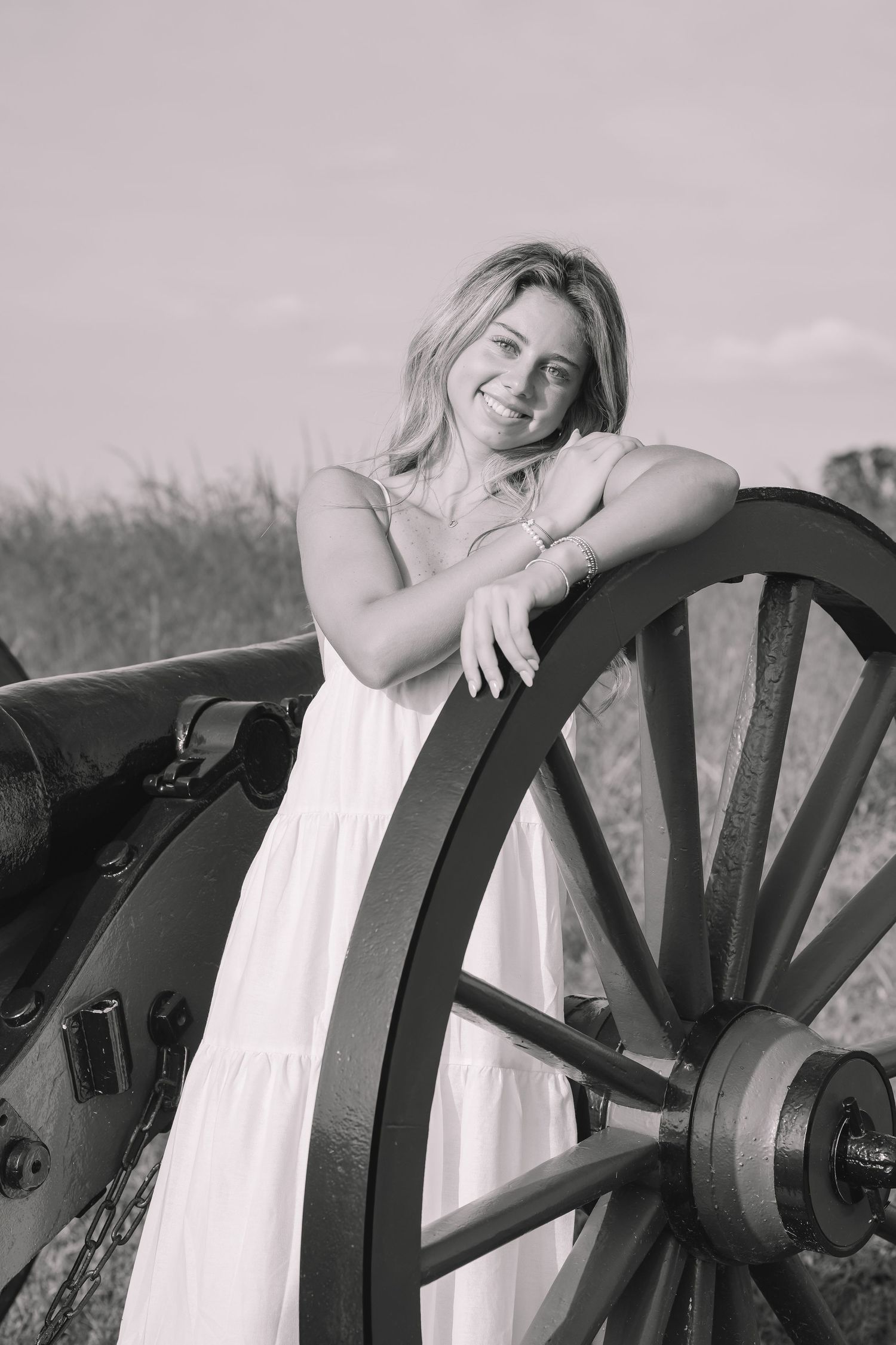 A black and white artistic photo series showing a graduate in white dress reclining on a vintage wooden wagon wheel in Manassas, Virginia.
