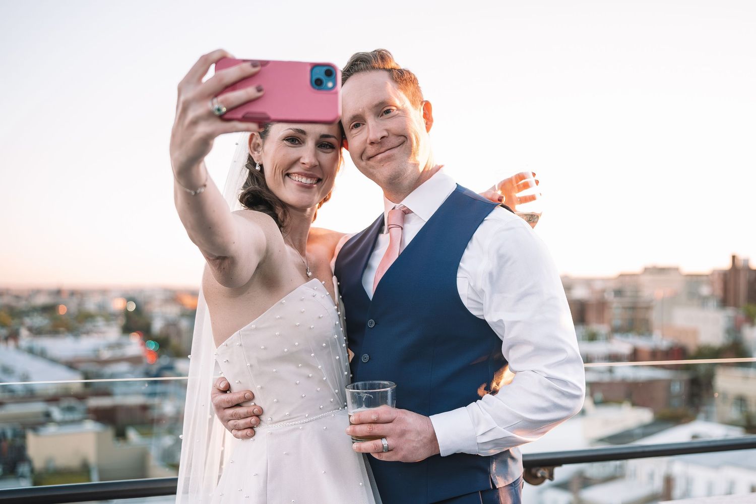 Wedding couple taking a selfie together on a rooftop terrace at sunset.