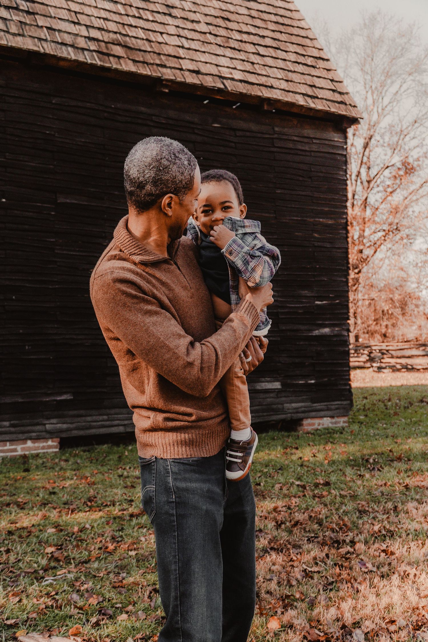 Tender parenting moment captured against rustic barn in warm autumn light.