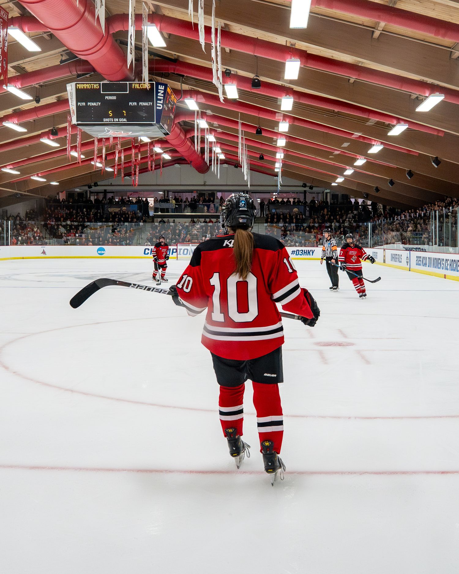 Ice hockey player wearing jersey number 10 in red and white stands on rink during indoor game with crowd in background.