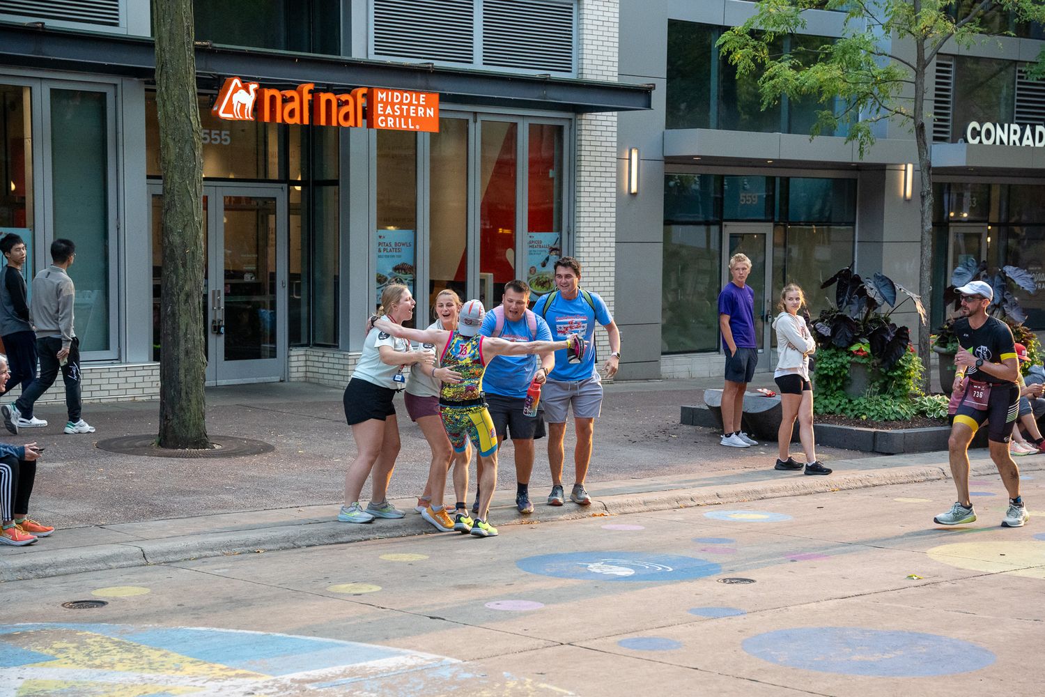People walking past a red fish restaurant while colorful chalk art decorates the sidewalk on a sunny day.