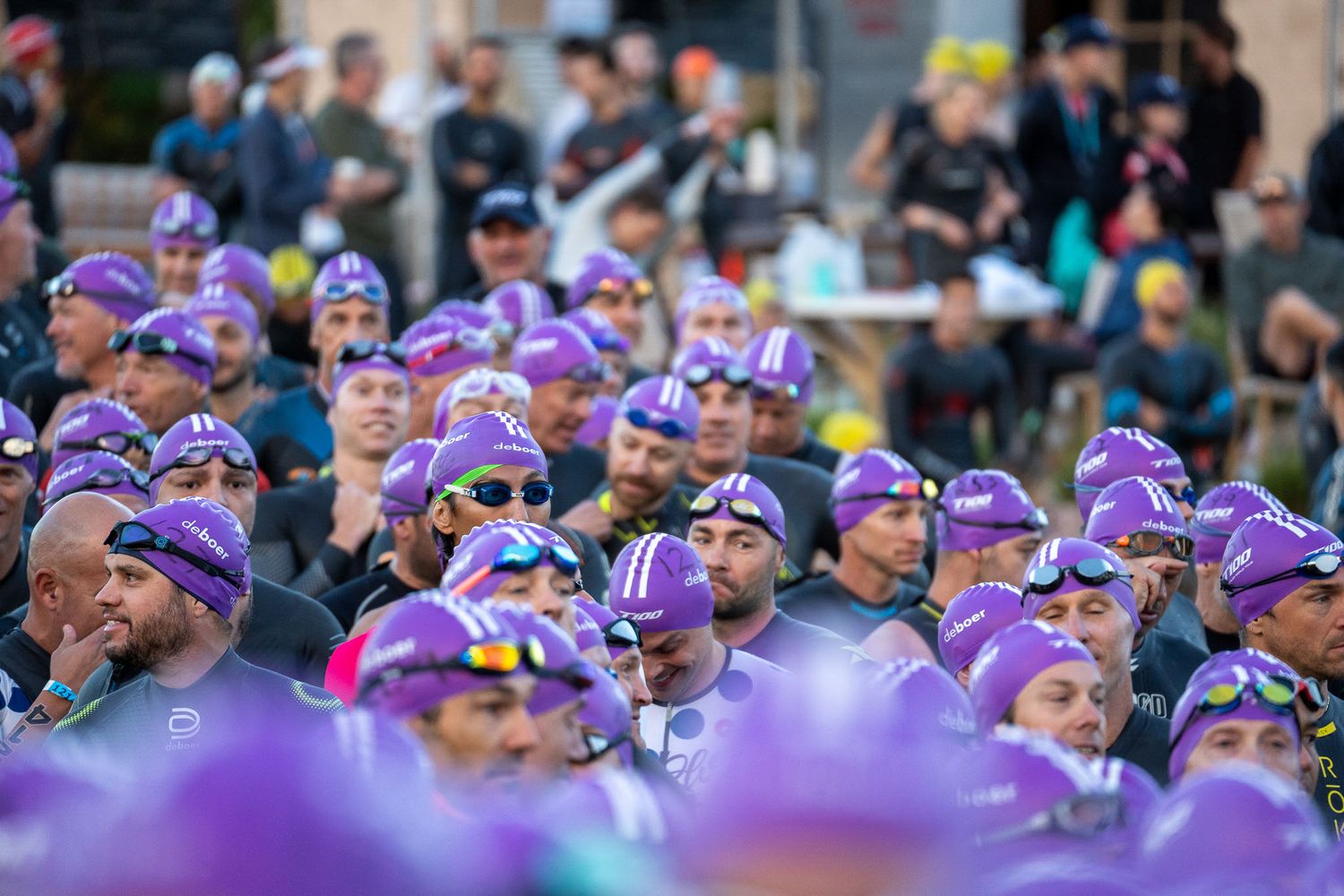 Large crowd of spectators wearing purple winter hats gather to watch an outdoor event.