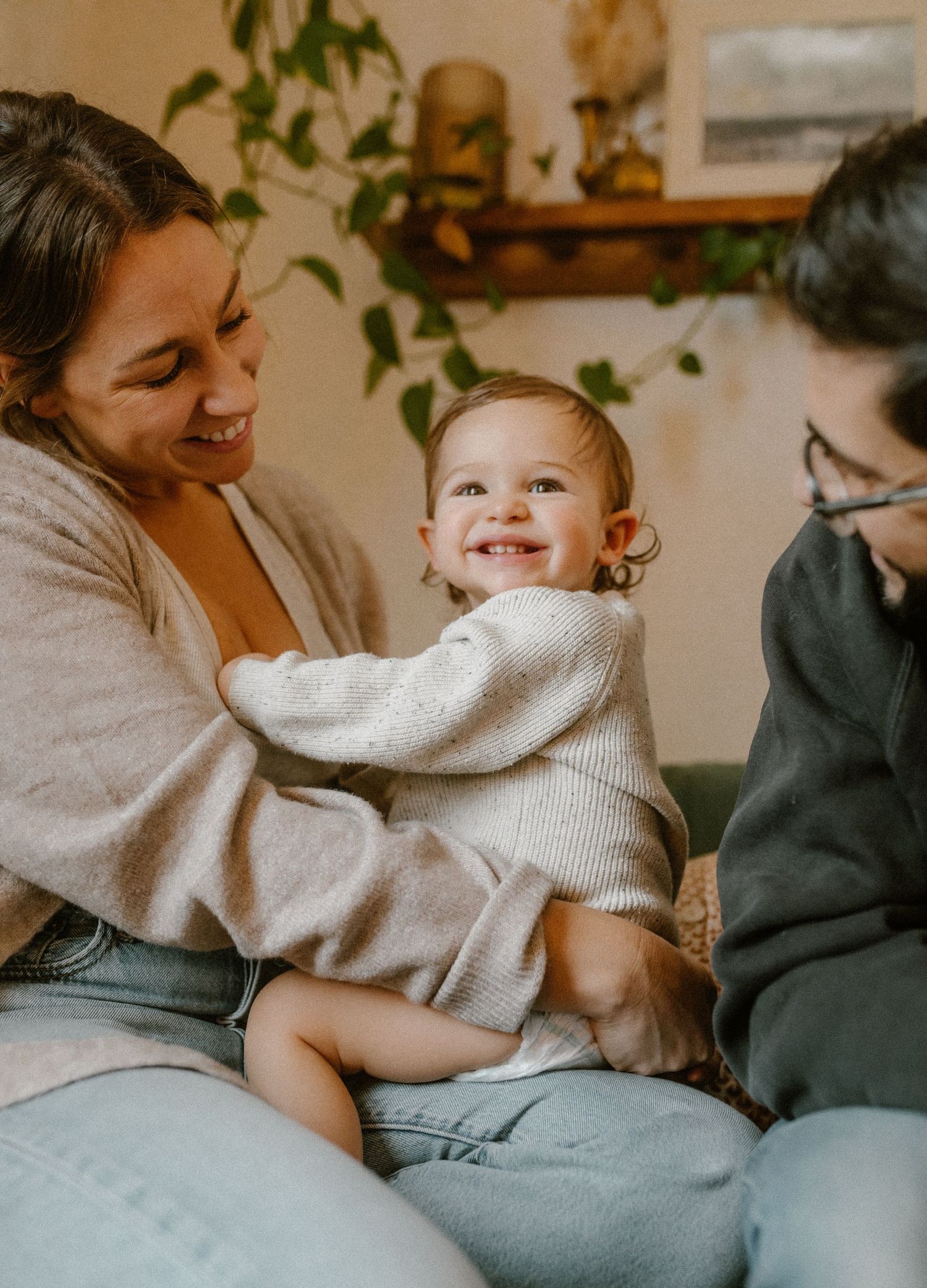 Joyful family moment on a green couch with decorative plants and artwork in background.