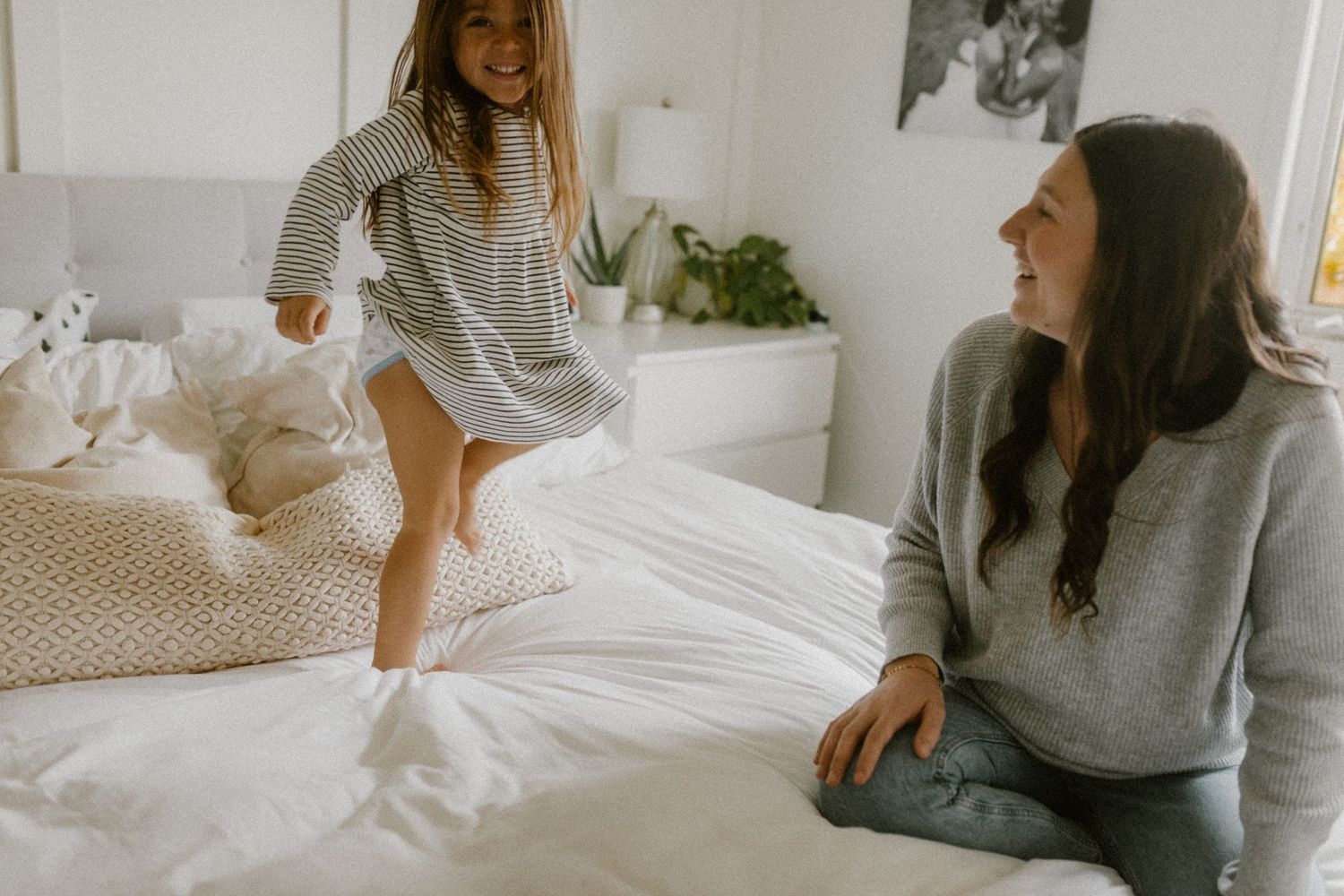 A playful scene of jumping on a white bed in a bright minimalist bedroom.