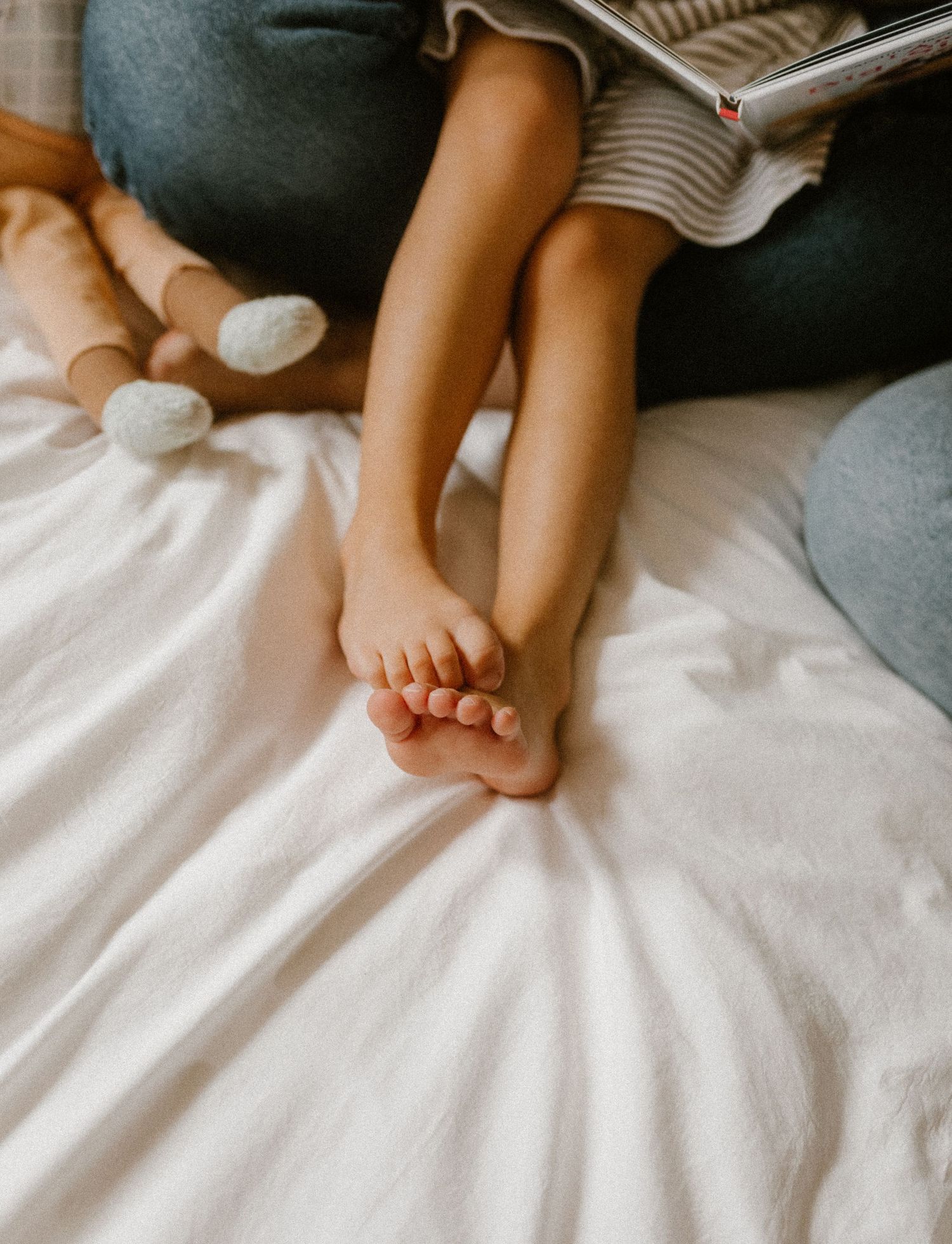 Close-up of bare feet scrunched up on white bedding in soft natural light.