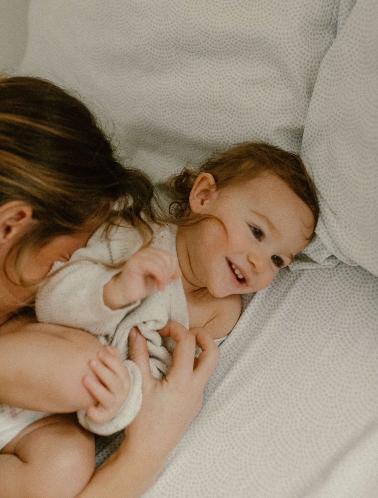 Intimate lifestyle photography capturing gentle moments of connection on white bedding.