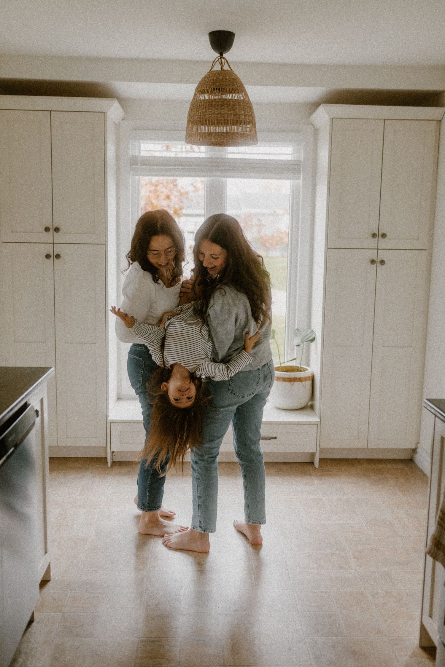 Playful queer family moment in a bright white kitchen with wooden floors and modern cabinetry.