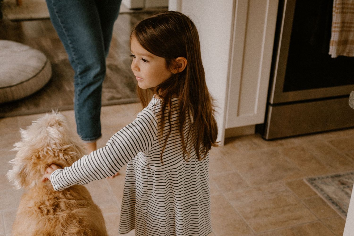 Child in striped dress reaching out to pet a furry dog.