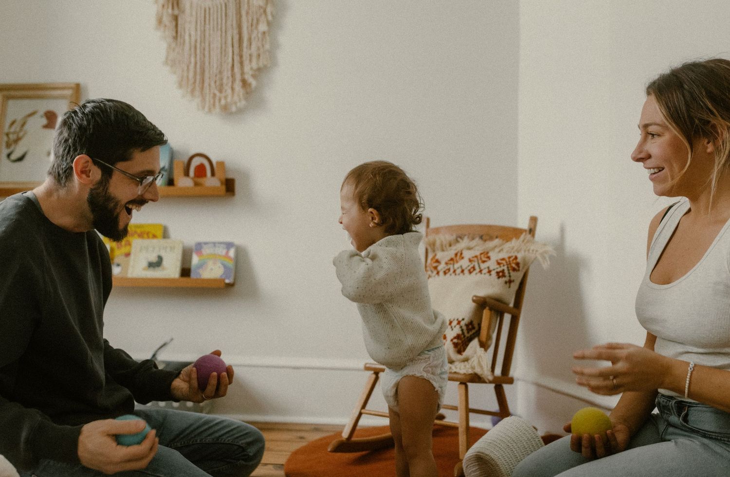 A family shares a playful moment together in a nursery decorated with macrame wall art.