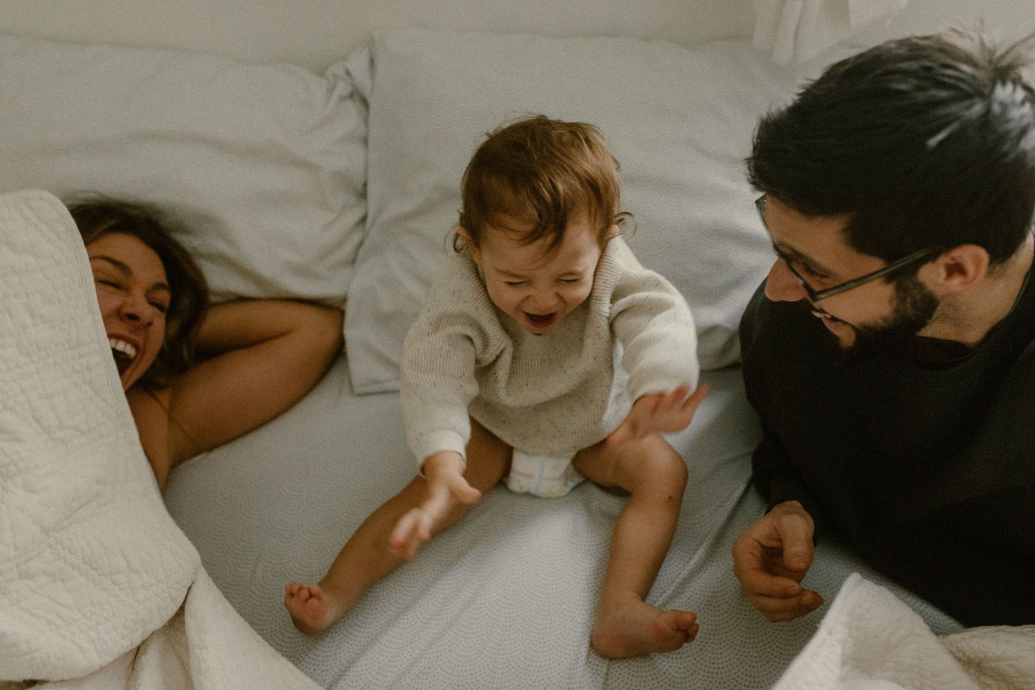 Joyful family moment captured on white bedding with natural lighting.