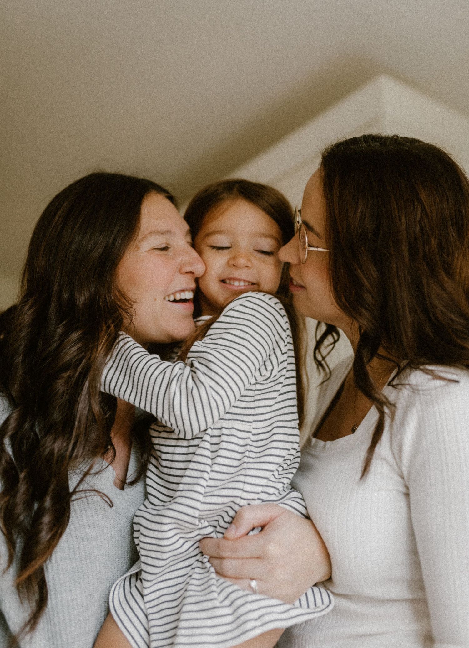 A joyful queer family moment of embrace and laughter in casual striped and white clothing.
