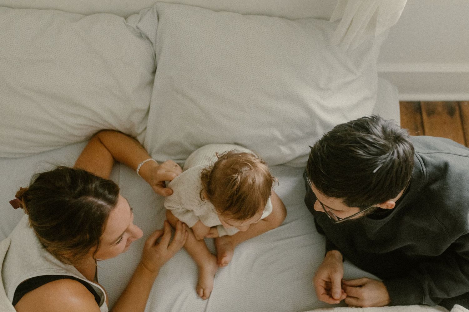 Tender family moment captured from above on white bedding showing closeness and connection.