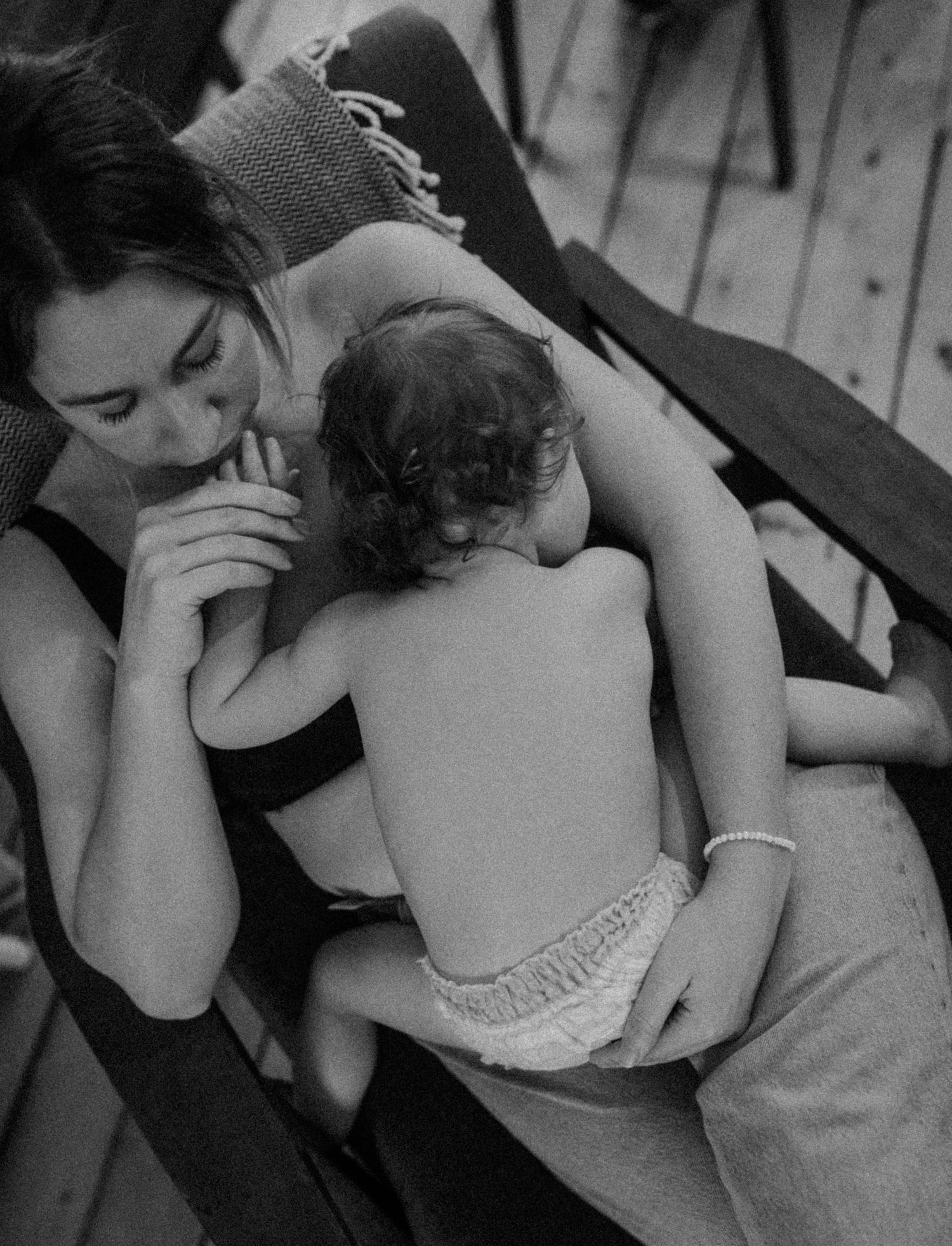 Black and white photograph capturing an intimate moment between parent and baby on wooden floor.