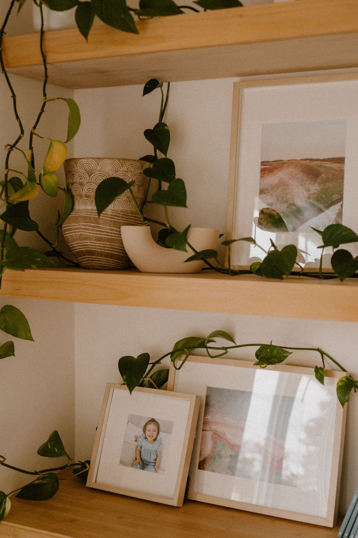 Wooden shelf decorated with plants, vases, and framed photographs in a cozy home setting.
