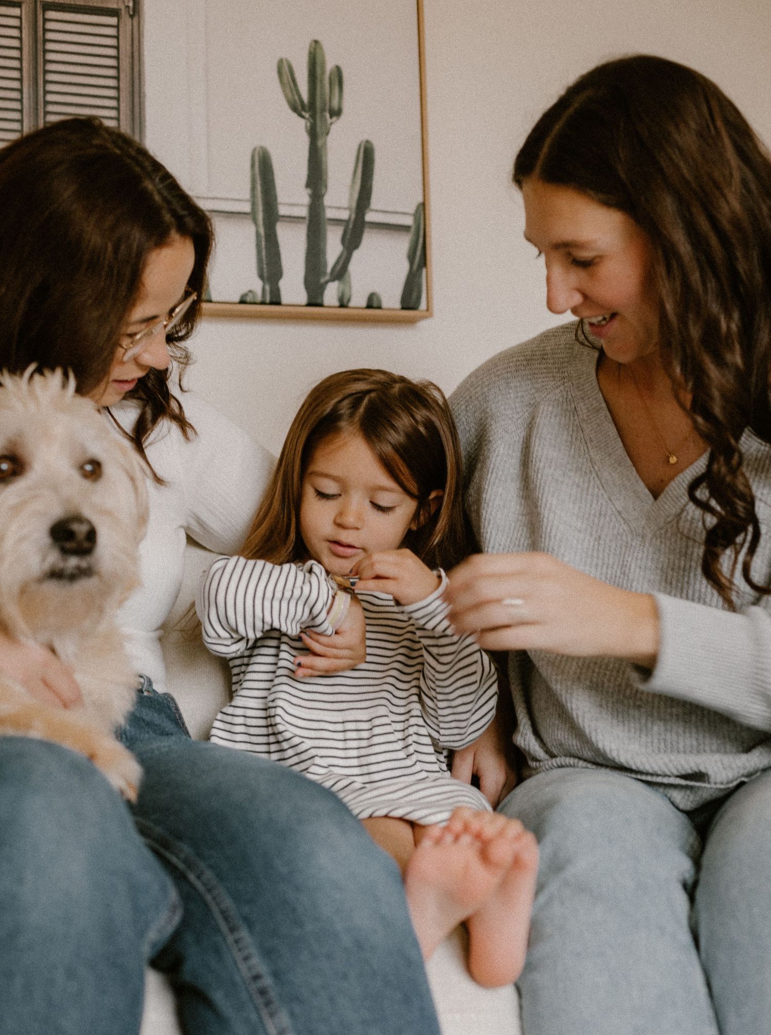 White fluffy dog joins queer family photo with cactus artwork in background.