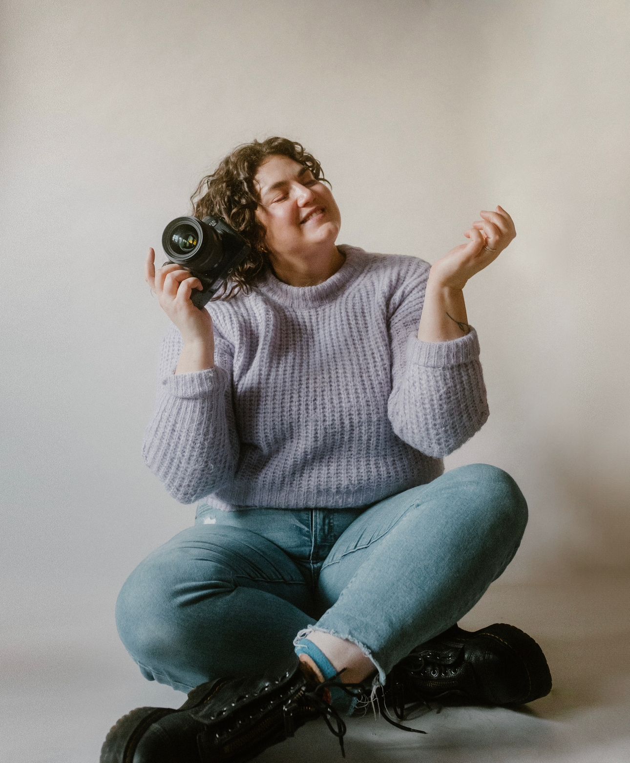 Photo of family and motherhood photographer holding a camera and smiling while wearing a lavender sweater and jeans