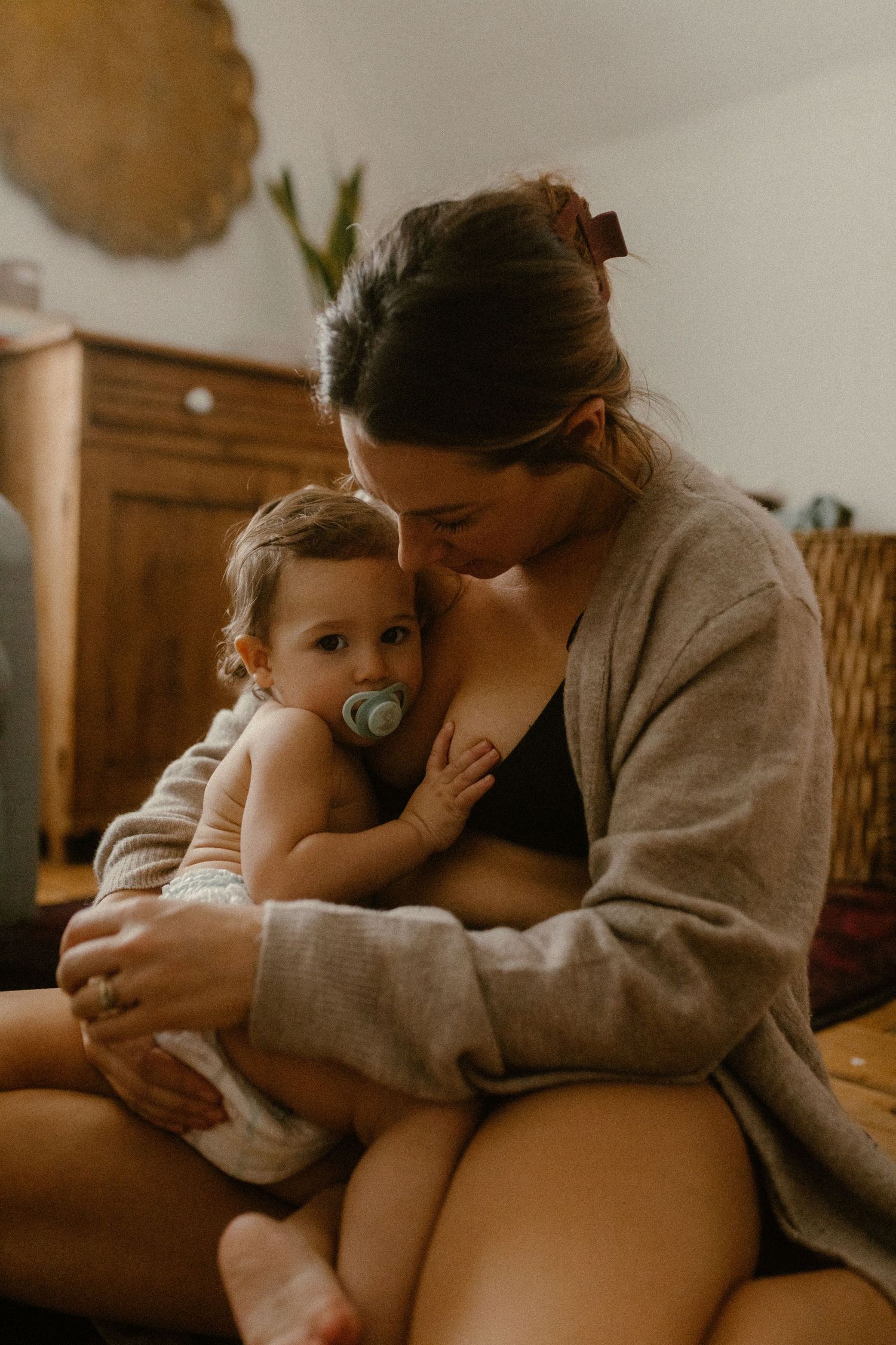 Tender nursing moment captured in warm tones with wooden furniture in background.