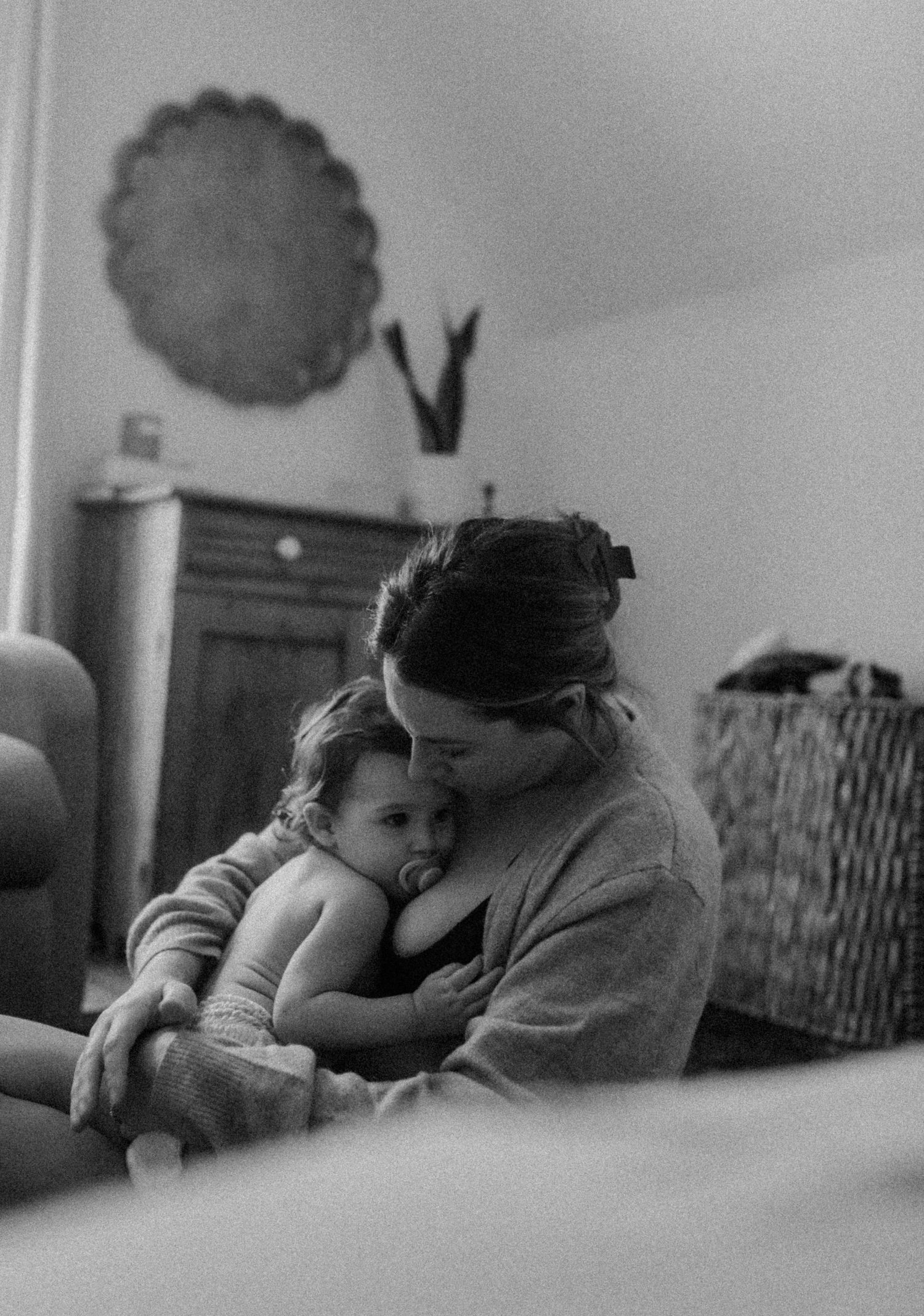 A tender black and white moment captured between parent and child as they cuddle together on a couch in soft lighting.