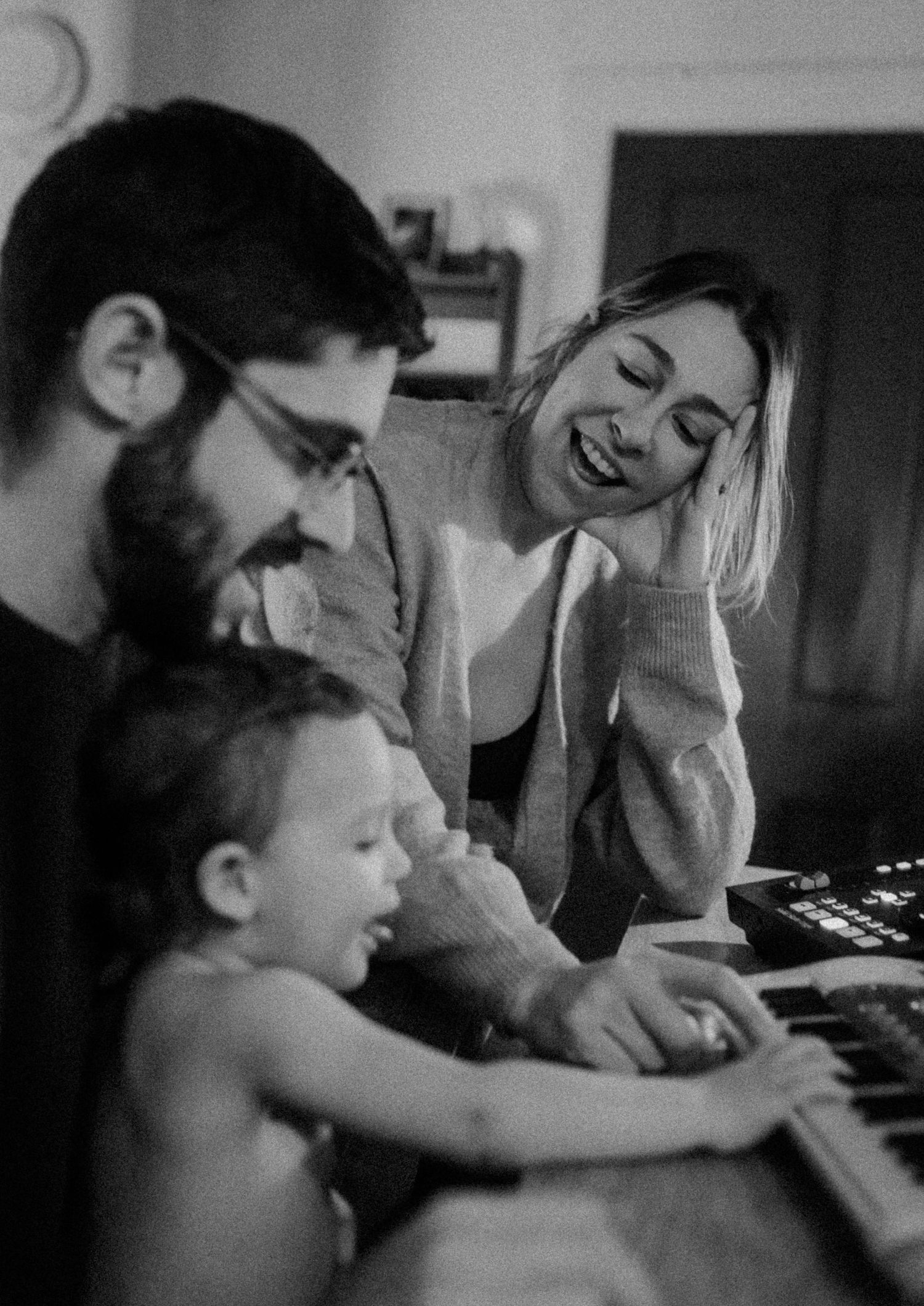Family enjoying time together at a piano in a candid black and white moment.