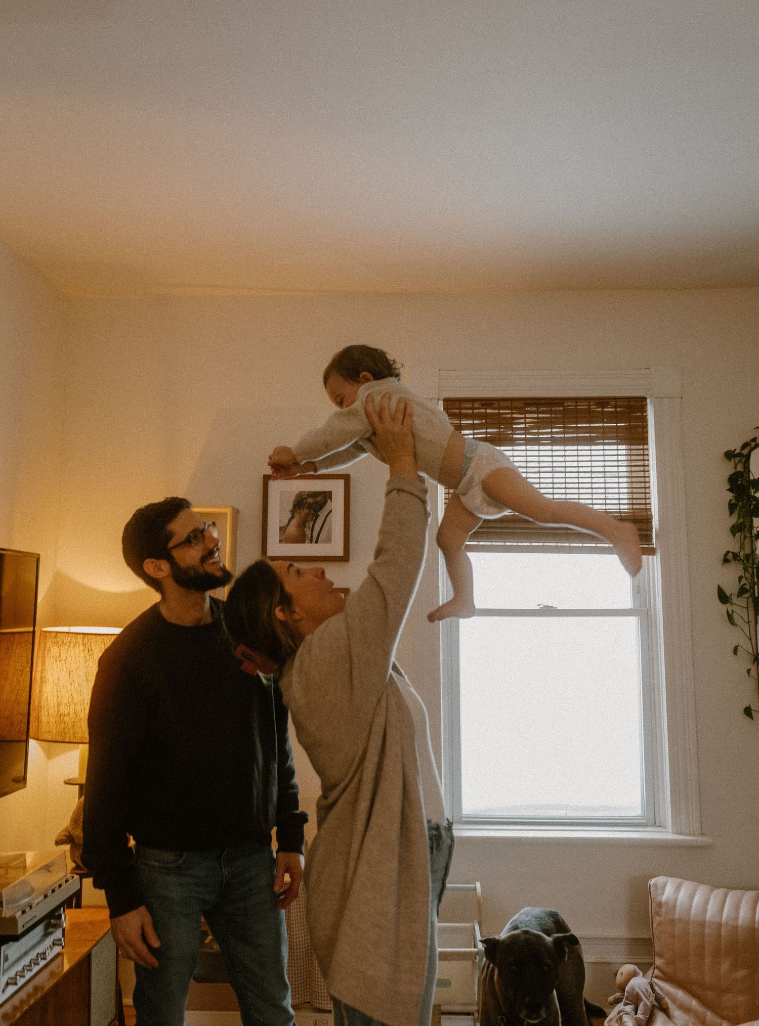 A playful family scene with warm lighting near a window with bamboo blinds.