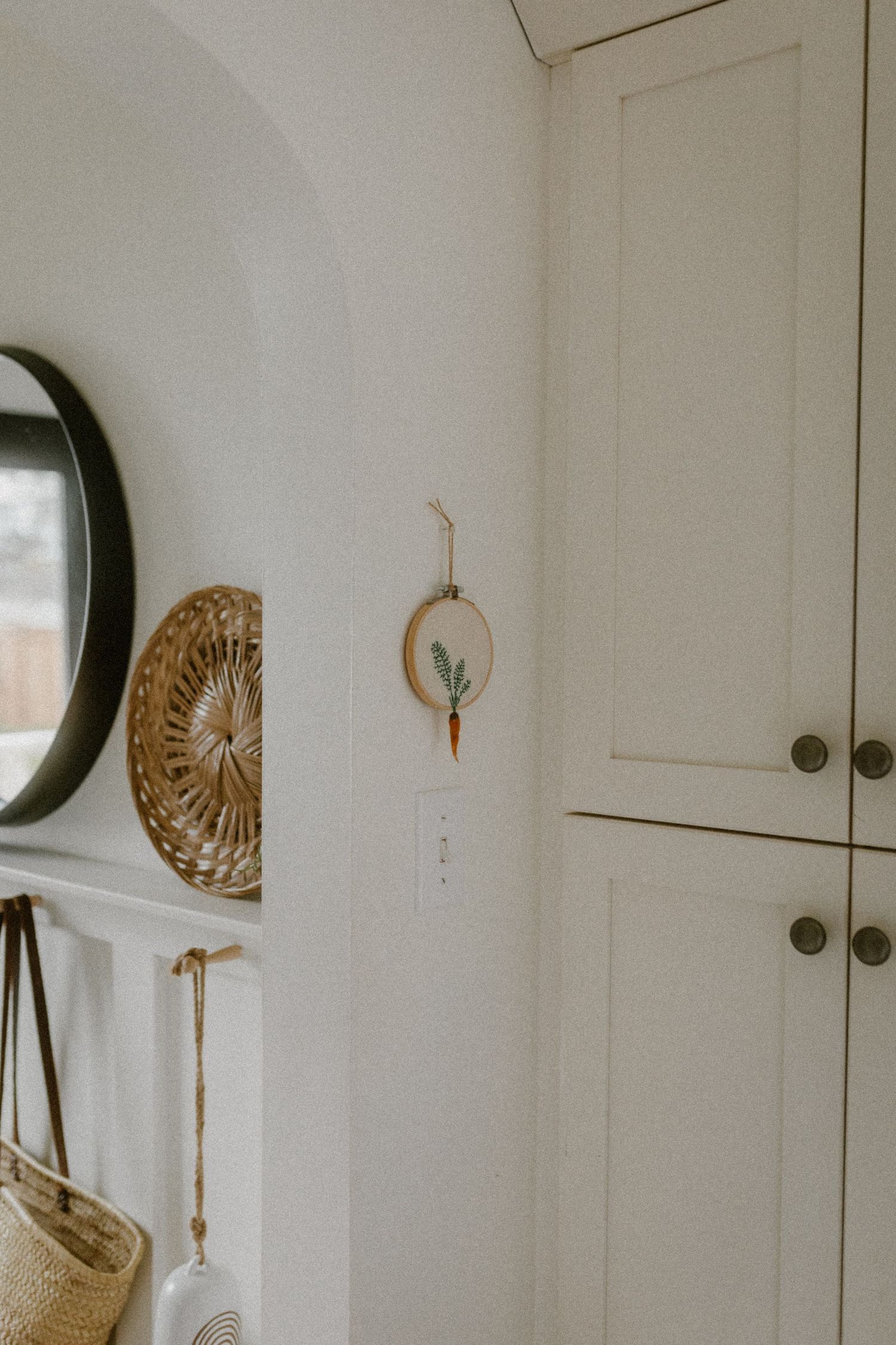 Modern minimalist entryway decor featuring round mirror, woven wall art, and built-in storage.