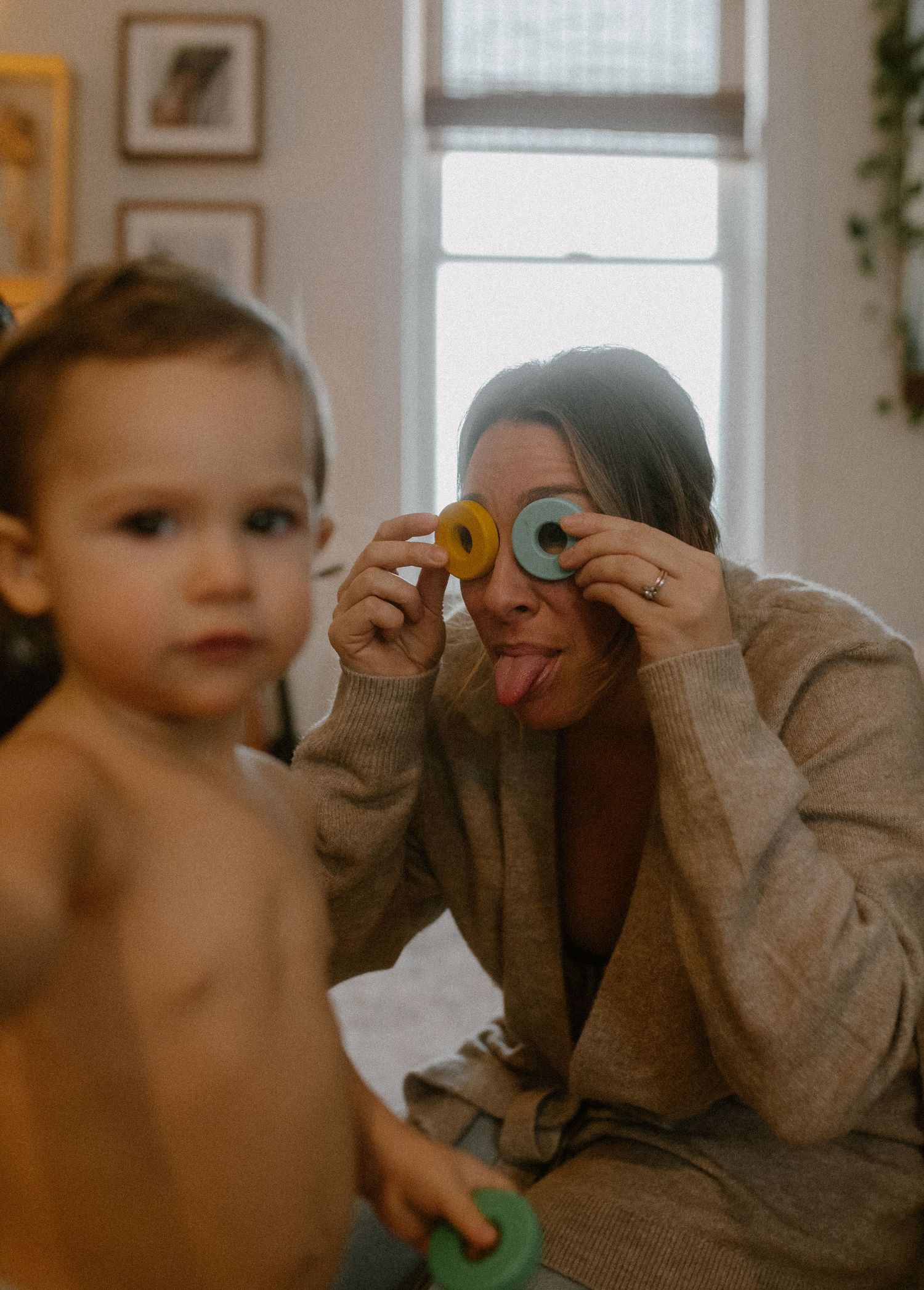 A playful moment as colorful plastic rings are held up to make silly faces in a sunlit room.