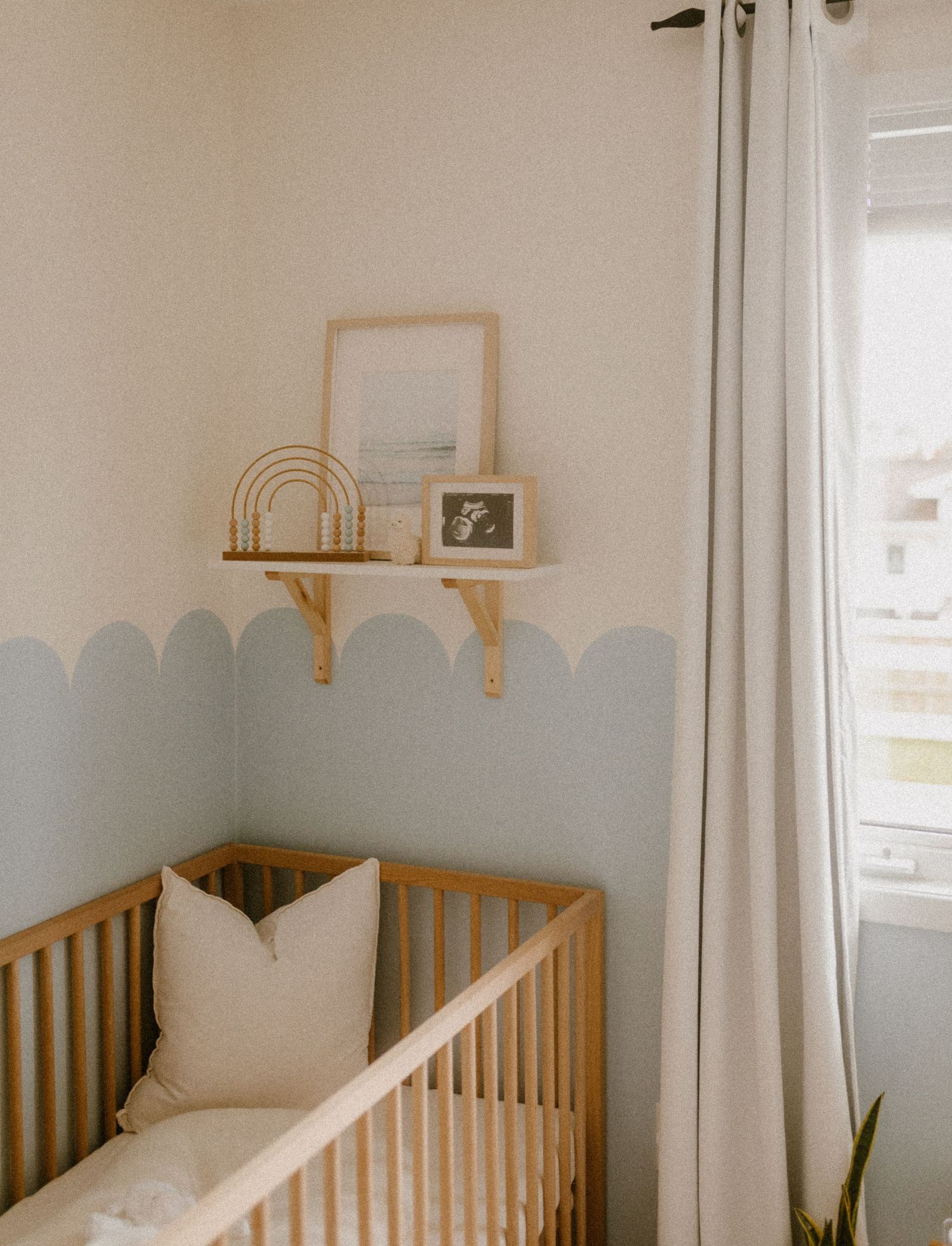 A minimalist nursery with wooden crib, scalloped wall detail and floating shelf with decorative items.