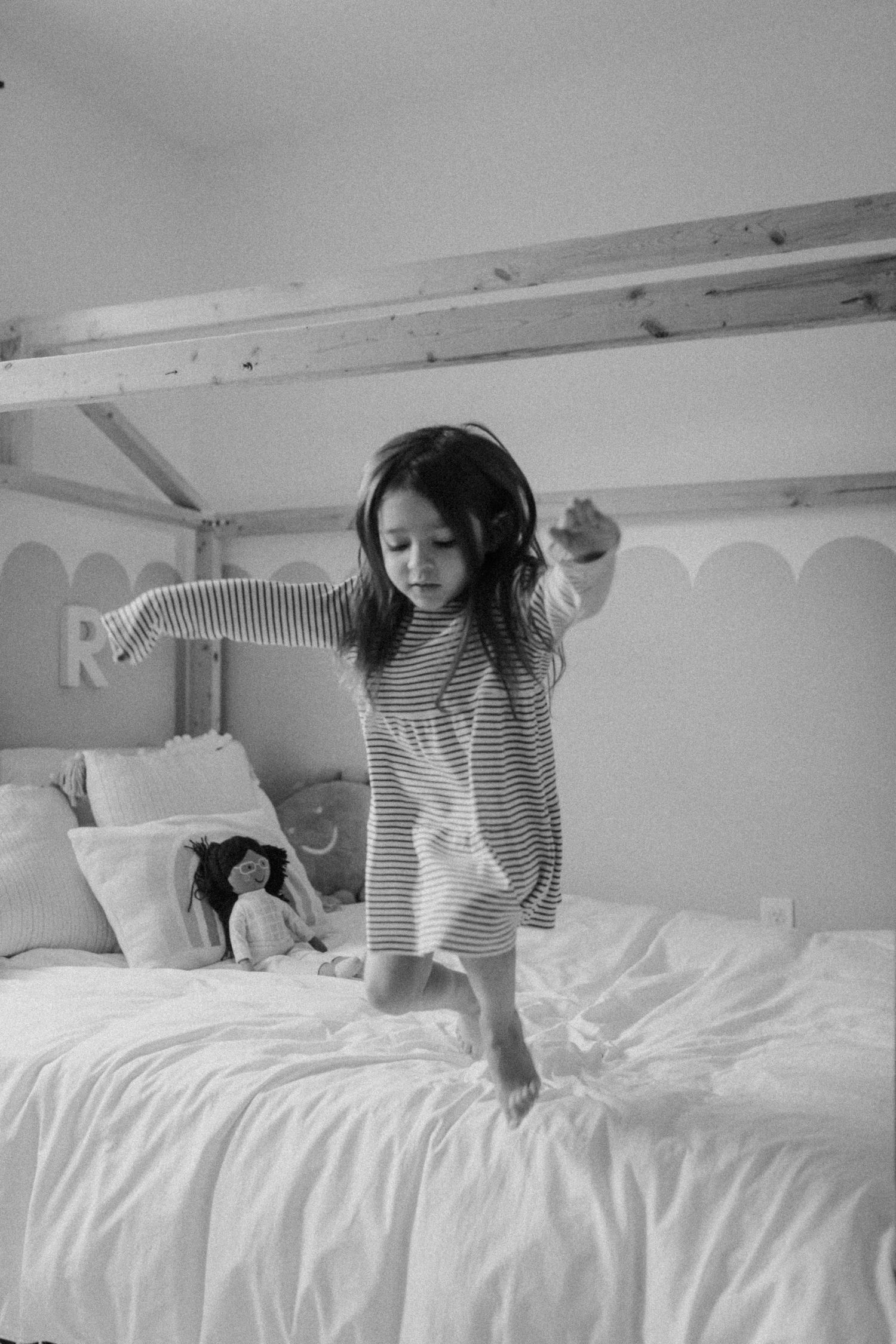 A child in striped pajamas dancing on a white bed with headphones.