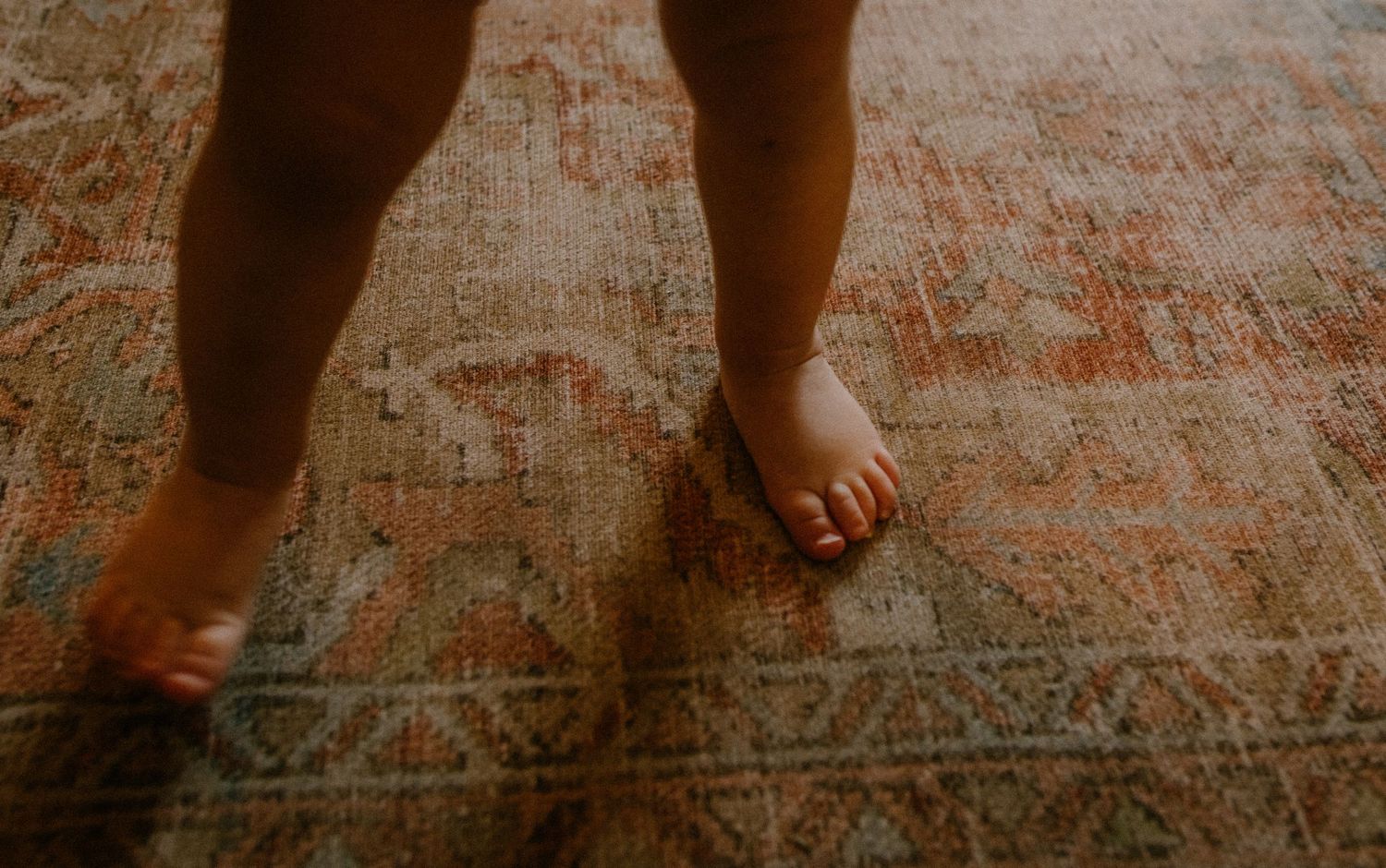 Bare feet stand on a patterned vintage area rug in warm lighting.