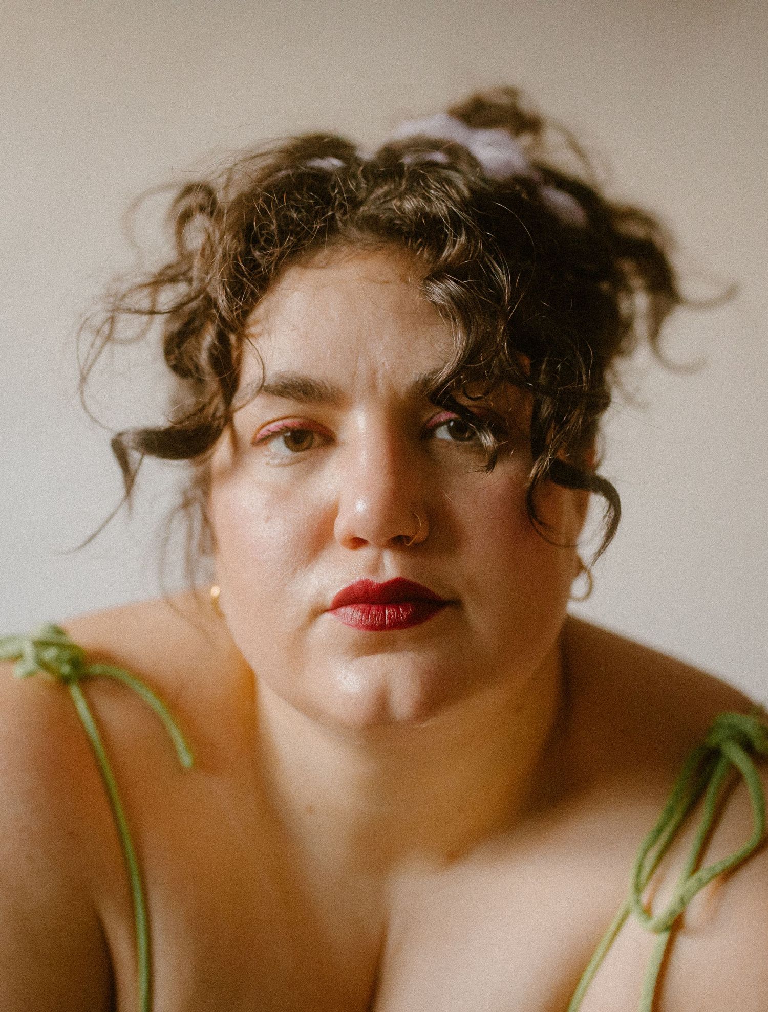 Close up portrait in warm lighting featuring someone in a green top with curly hair and red lipstick.
