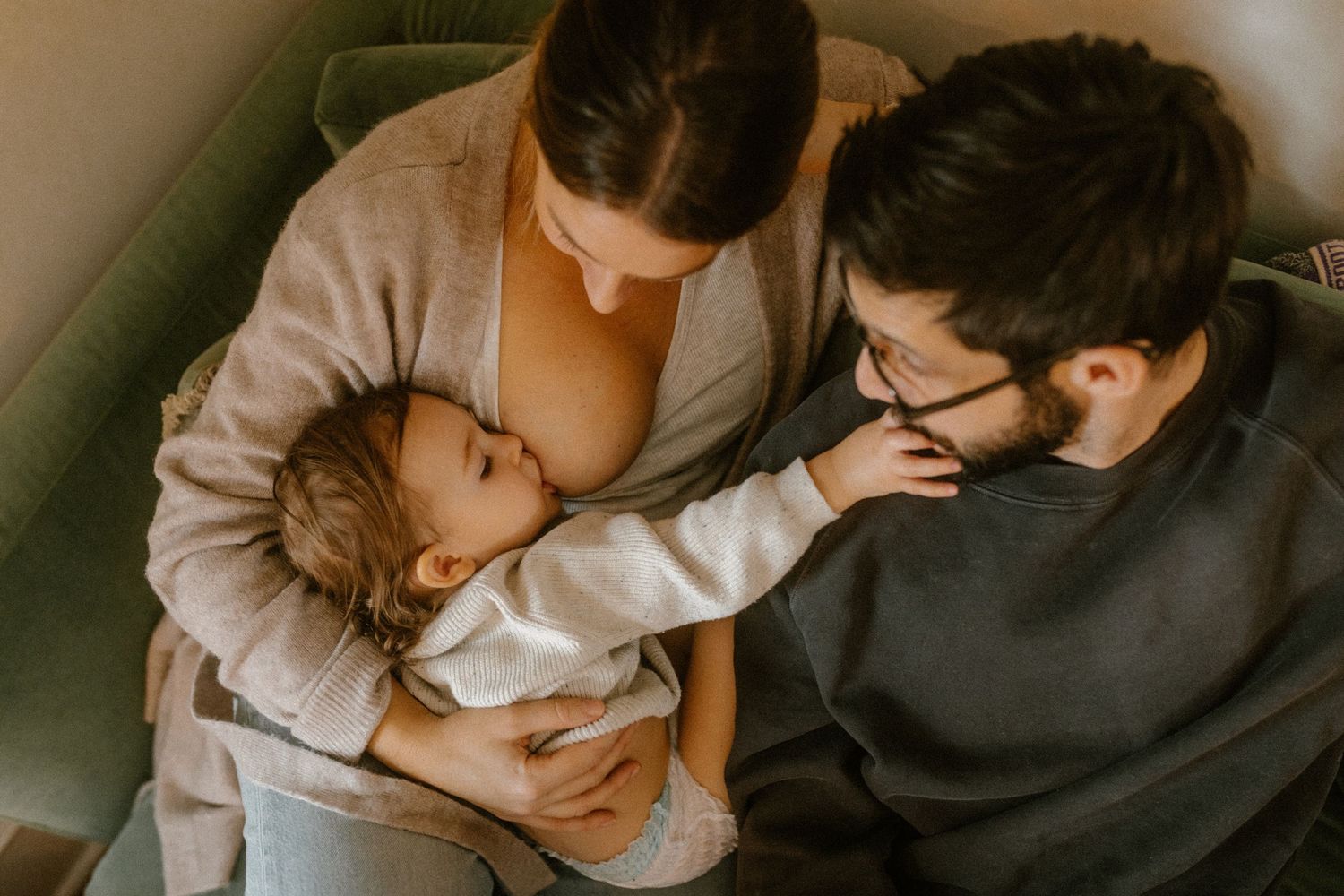 Warm-toned intimate family moment captured on a green couch in a cozy living room.