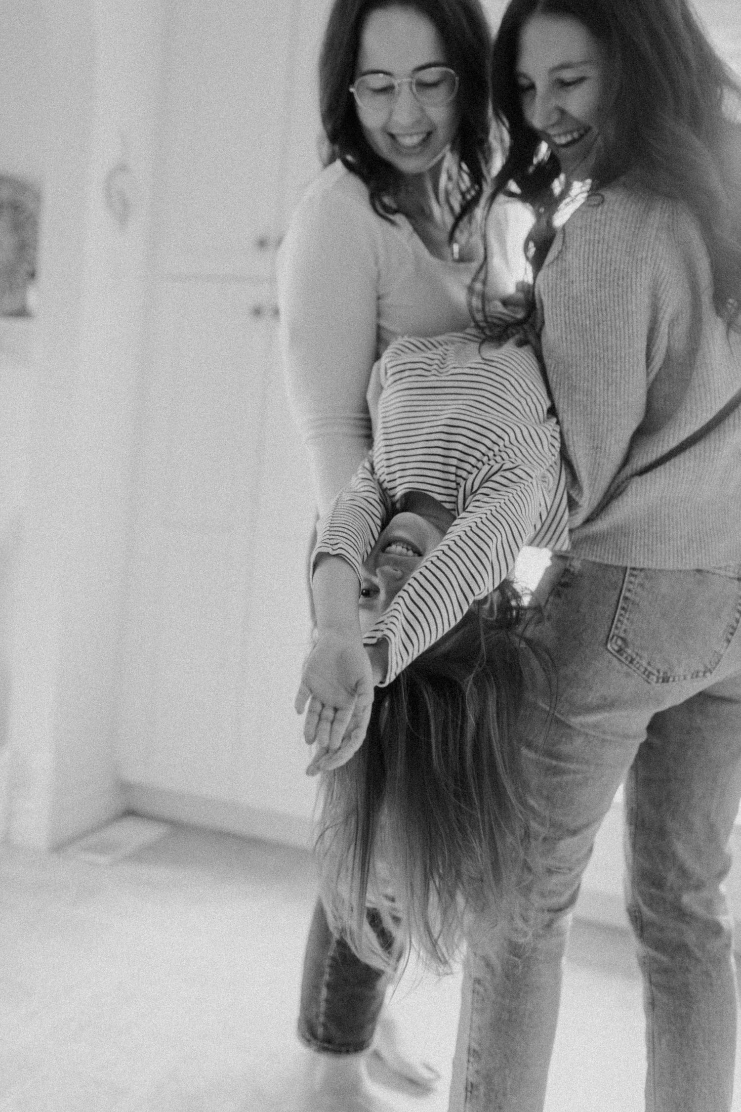 A candid black and white photo capturing a playful moment of swinging their daughter and laughter indoors.
