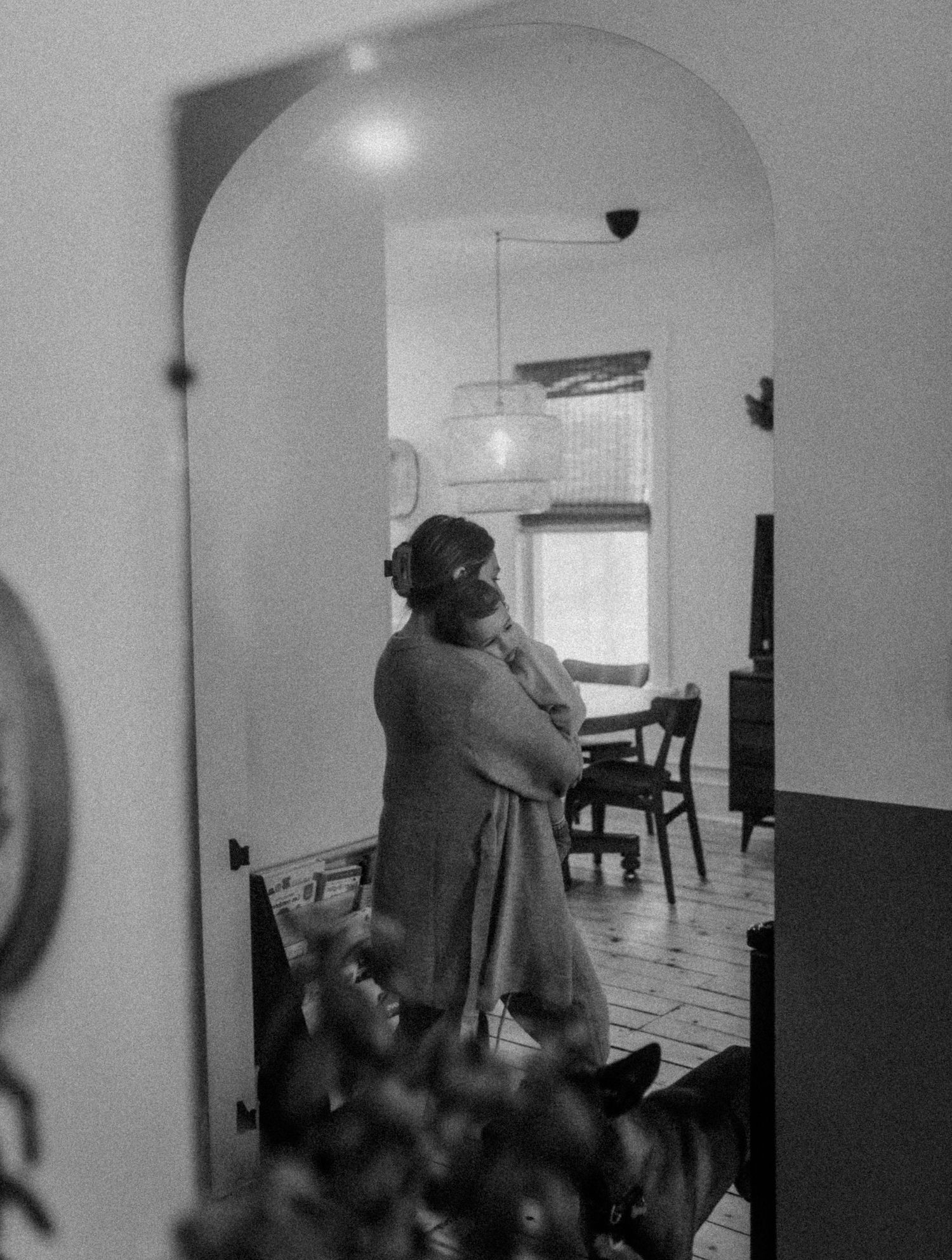 A gentle embrace between parent and child captured in black and white through an archway.