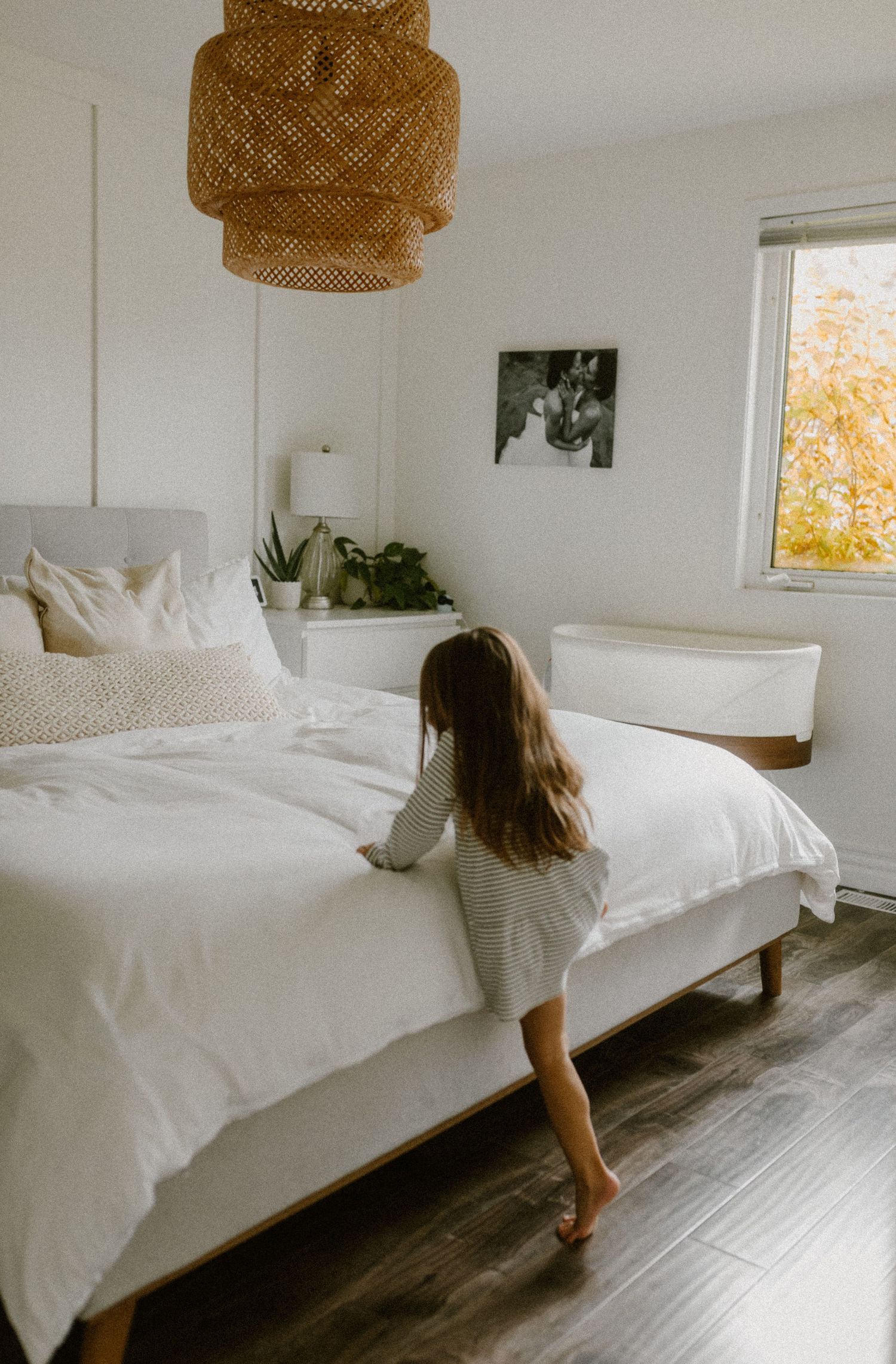 A minimal white bedroom with rattan pendant light and autumn view through the window.